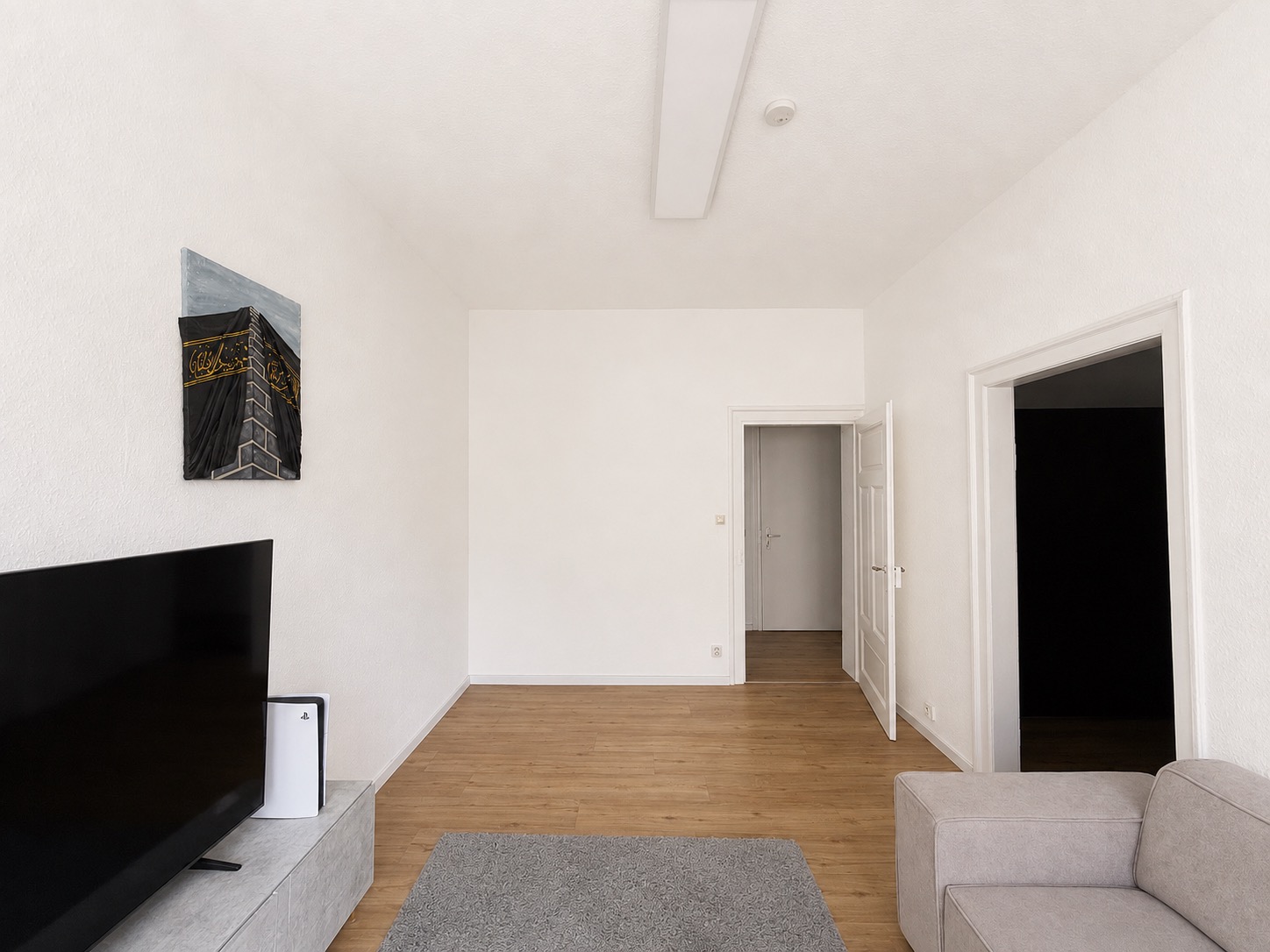 Helles Wohnzimmer mit Fernseher, grauem Teppich, Sofa und zwei offenen Türen.