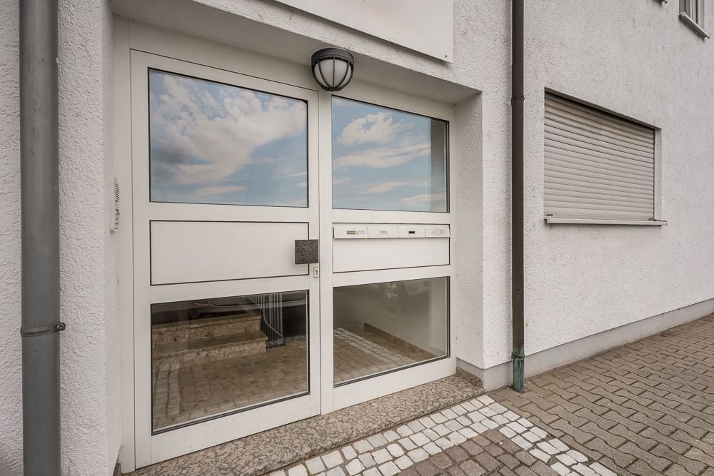 Weiße Hauseingangstür mit Glas und Briefkästen, daneben ein Fenster mit Rollladen.
