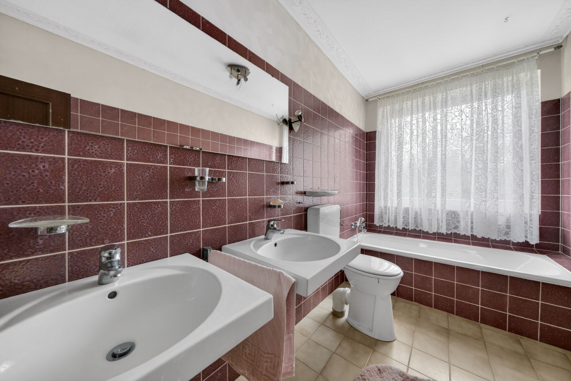 Badezimmer mit zwei Waschbecken, Toilette, Badewanne und Fenster mit Vorhang.