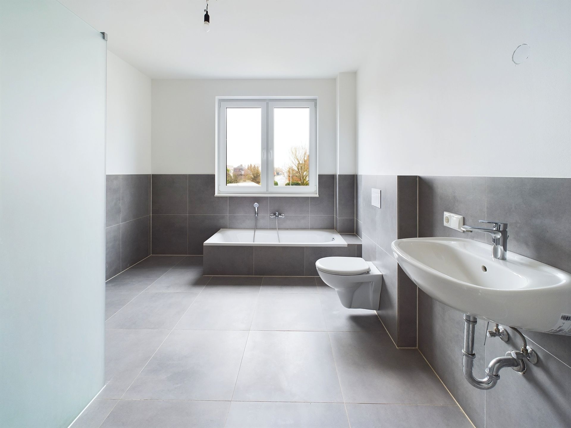 Modernes Badezimmer mit grauen Fliesen, Badewanne, Wand-WC und Waschbecken.