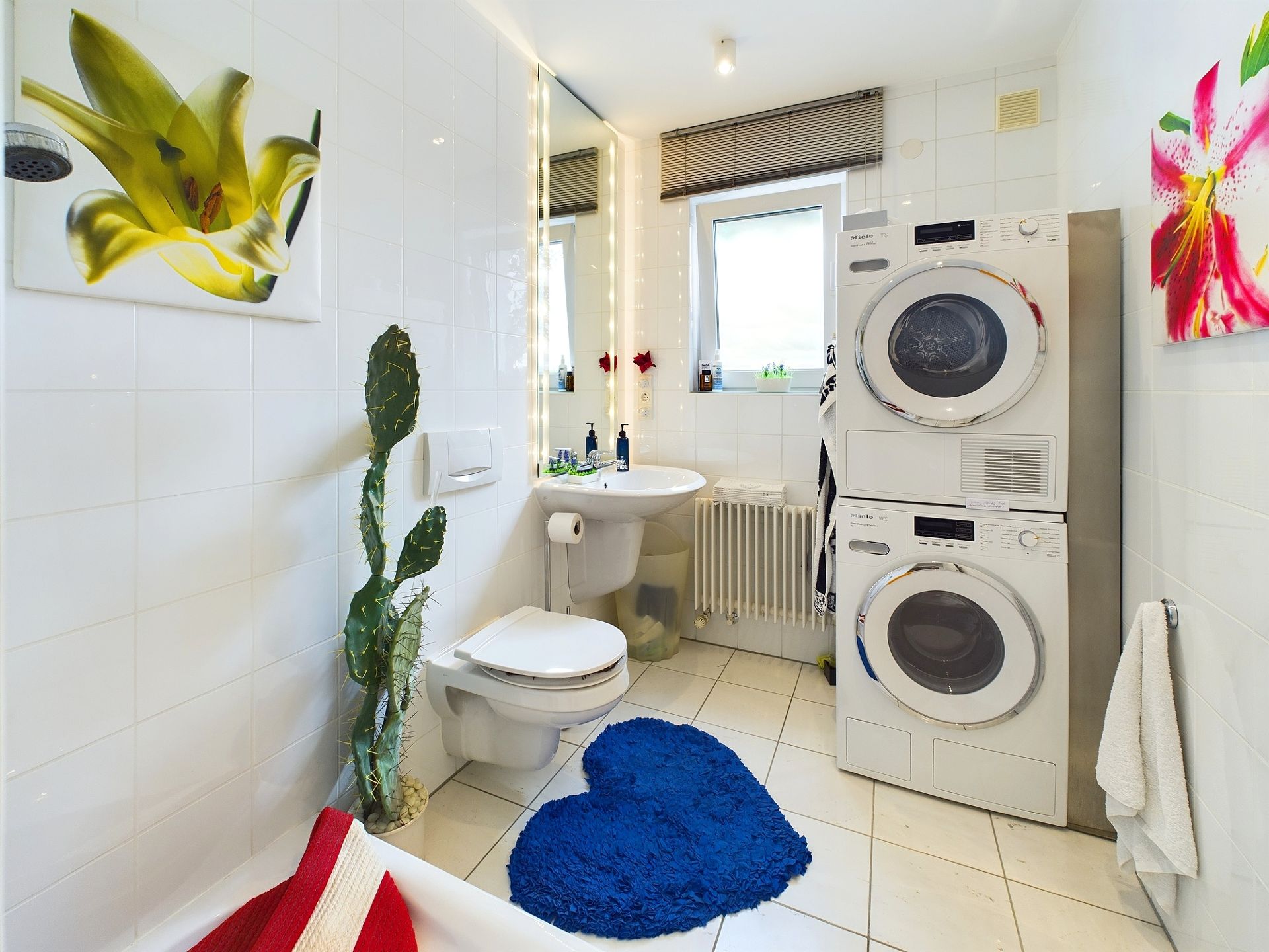 Helles Badezimmer mit Waschmaschine, Trockner, Toilette, Waschbecken, Pflanzen und blauer Herzmatte.