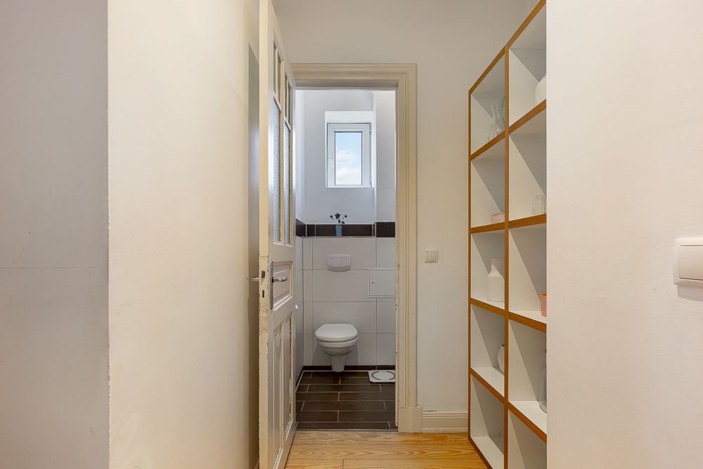 Blick durch den Flur auf ein kleines Badezimmer mit Toilette und Fenster.