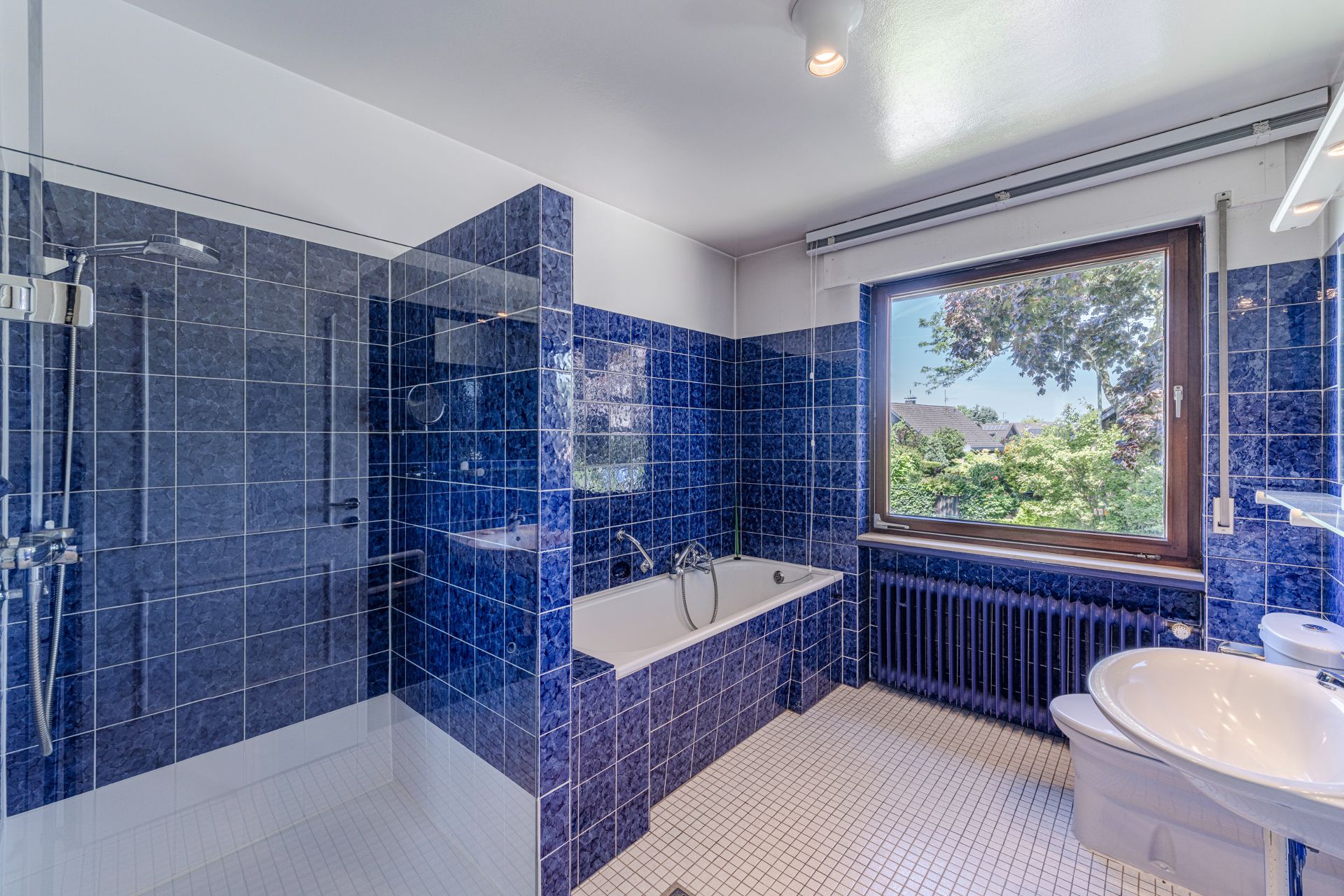 Badezimmer mit blauen Fliesen, Dusche, Badewanne, Waschbecken und großem Fenster.