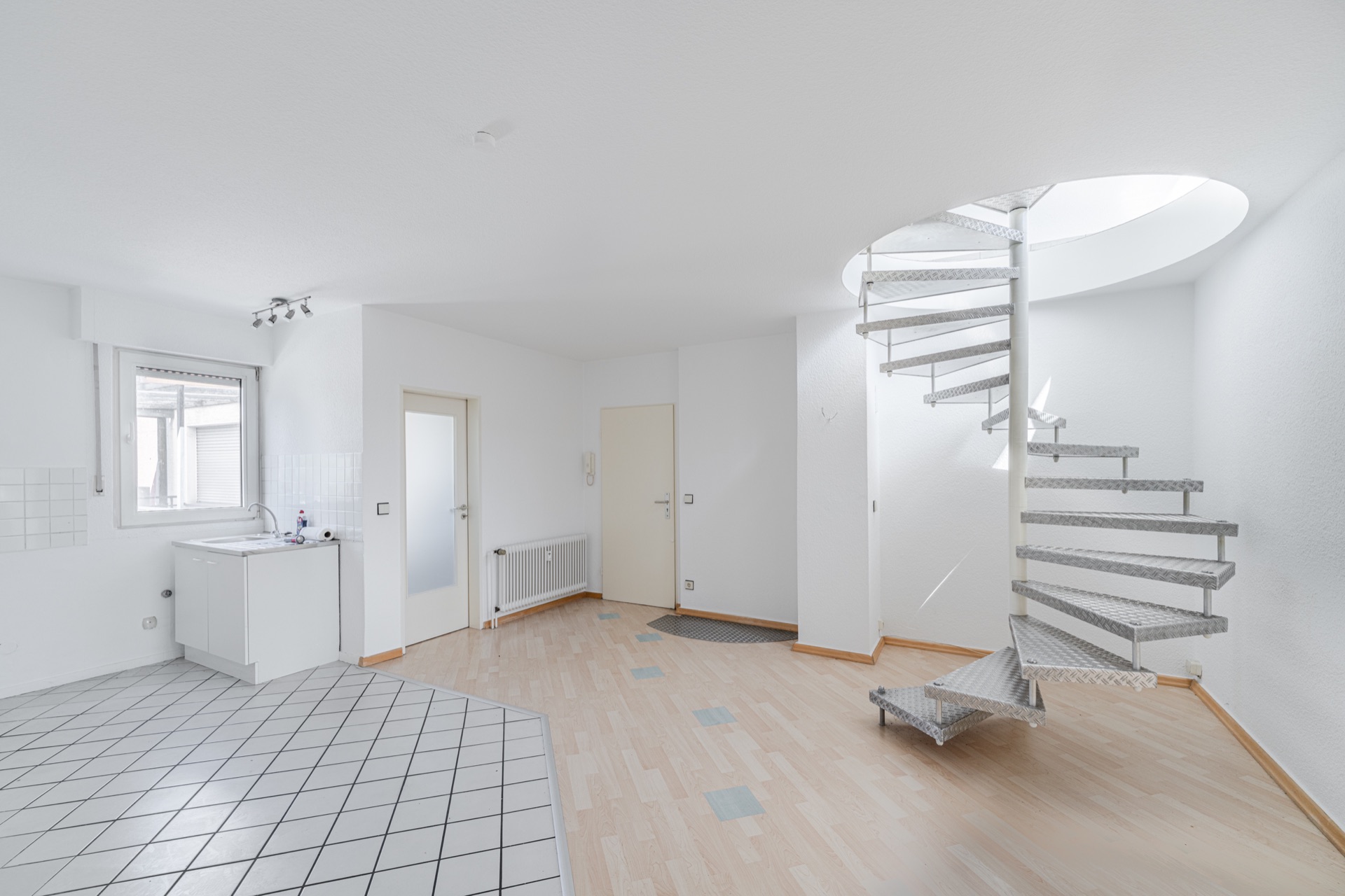 Helles Zimmer mit offener Küche und moderner Wendeltreppe aus Metall.