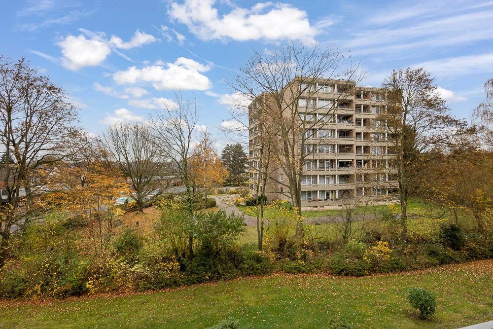 Mehrstöckiges Wohnhaus mit Balkonen, umgeben von Bäumen und Wiese an einem klaren Tag.