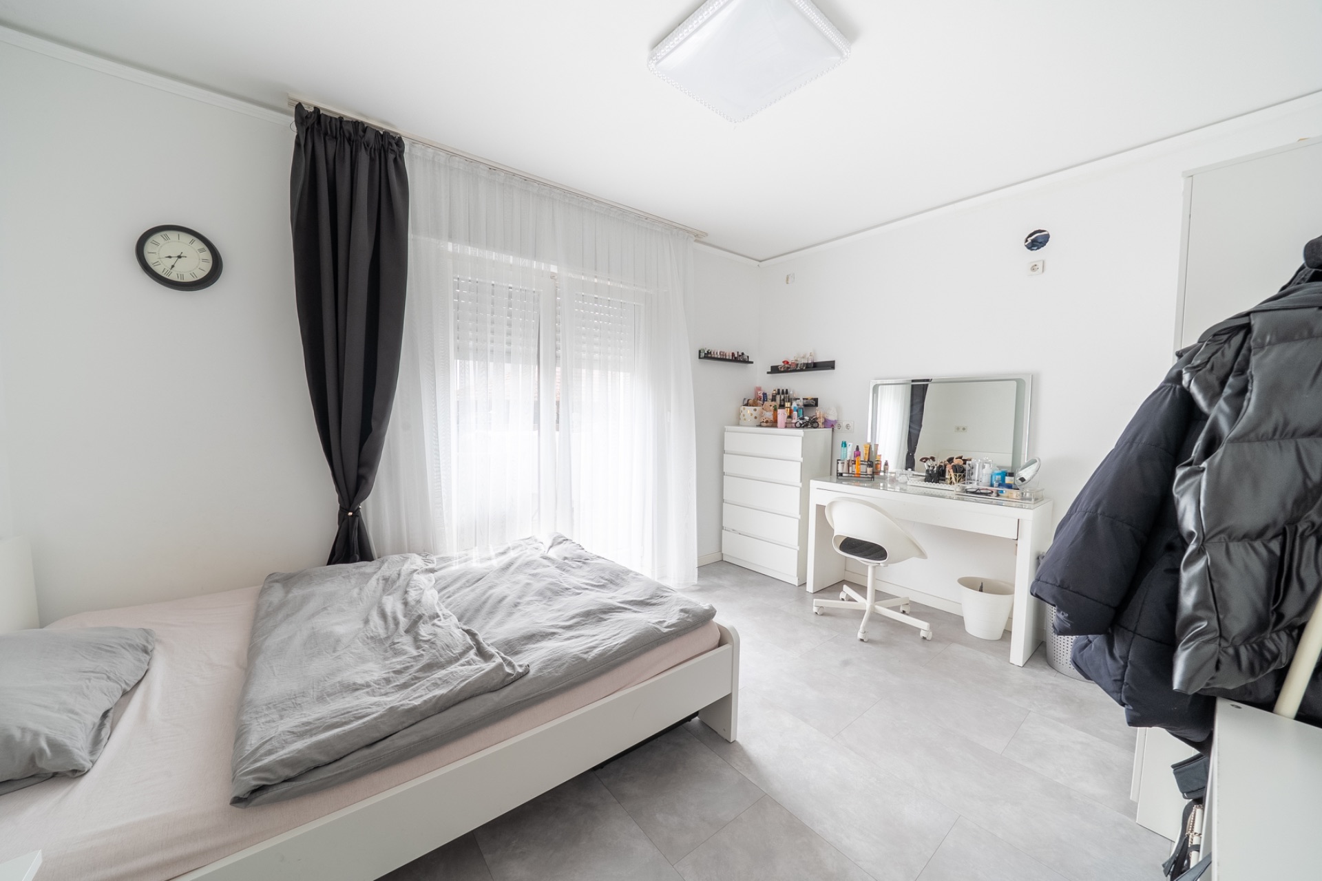 Helles Schlafzimmer mit Bett, Schminktisch, Kommode und Garderobe an der Wand.