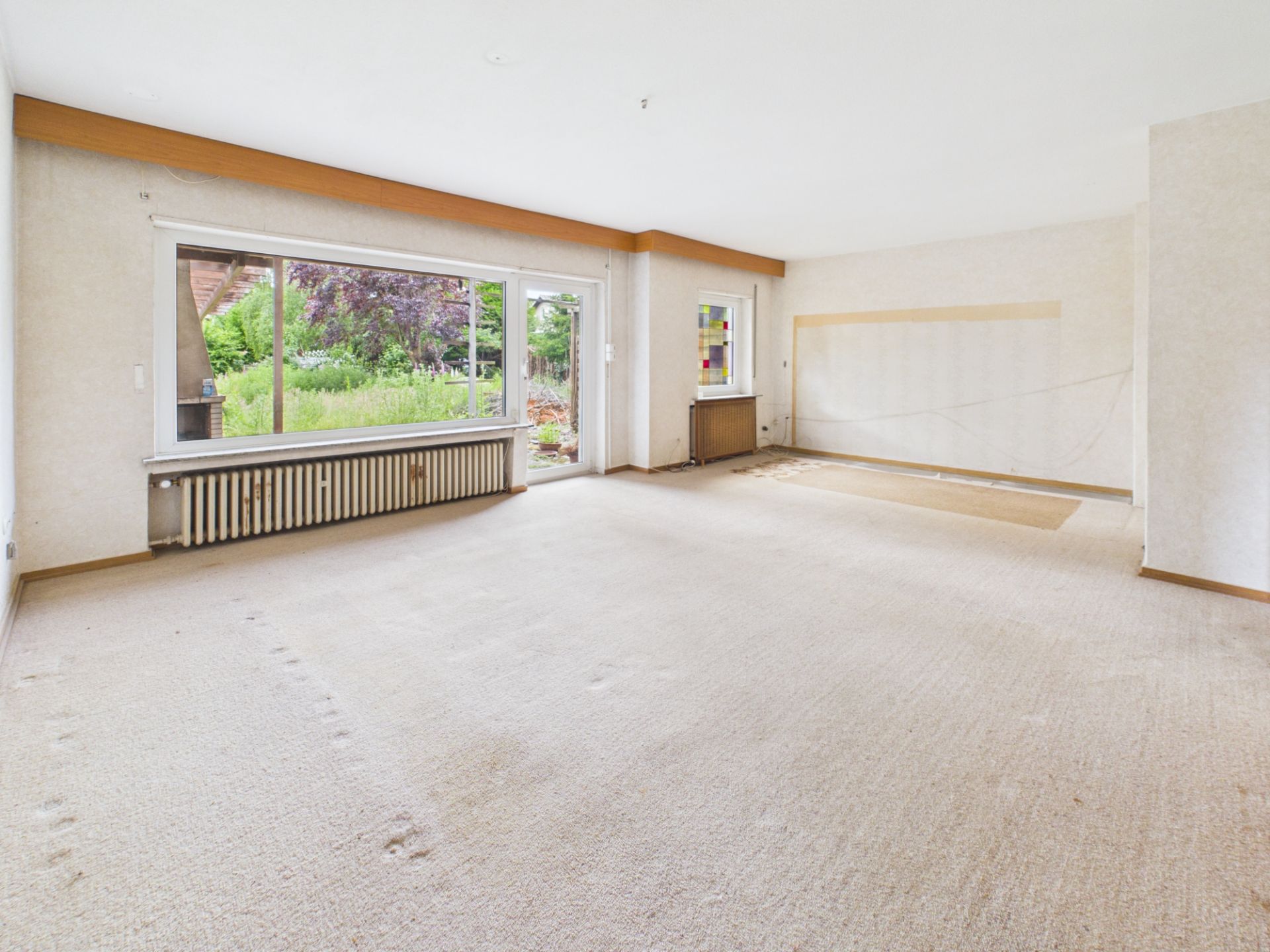 Leeres Wohnzimmer mit großem Fenster und Blick in den Garten.