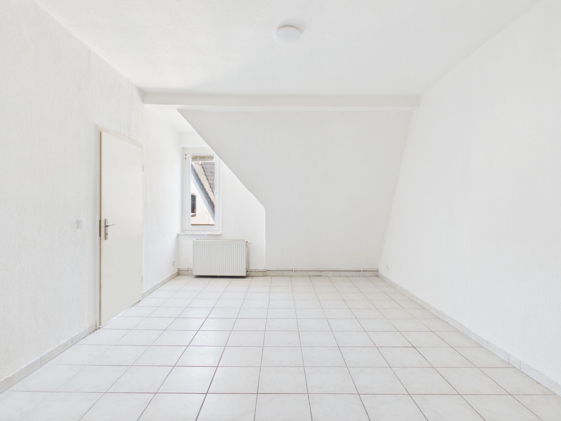 Leerer, weißer Raum mit Fliesenboden, Fenster, Tür und Heizkörper.