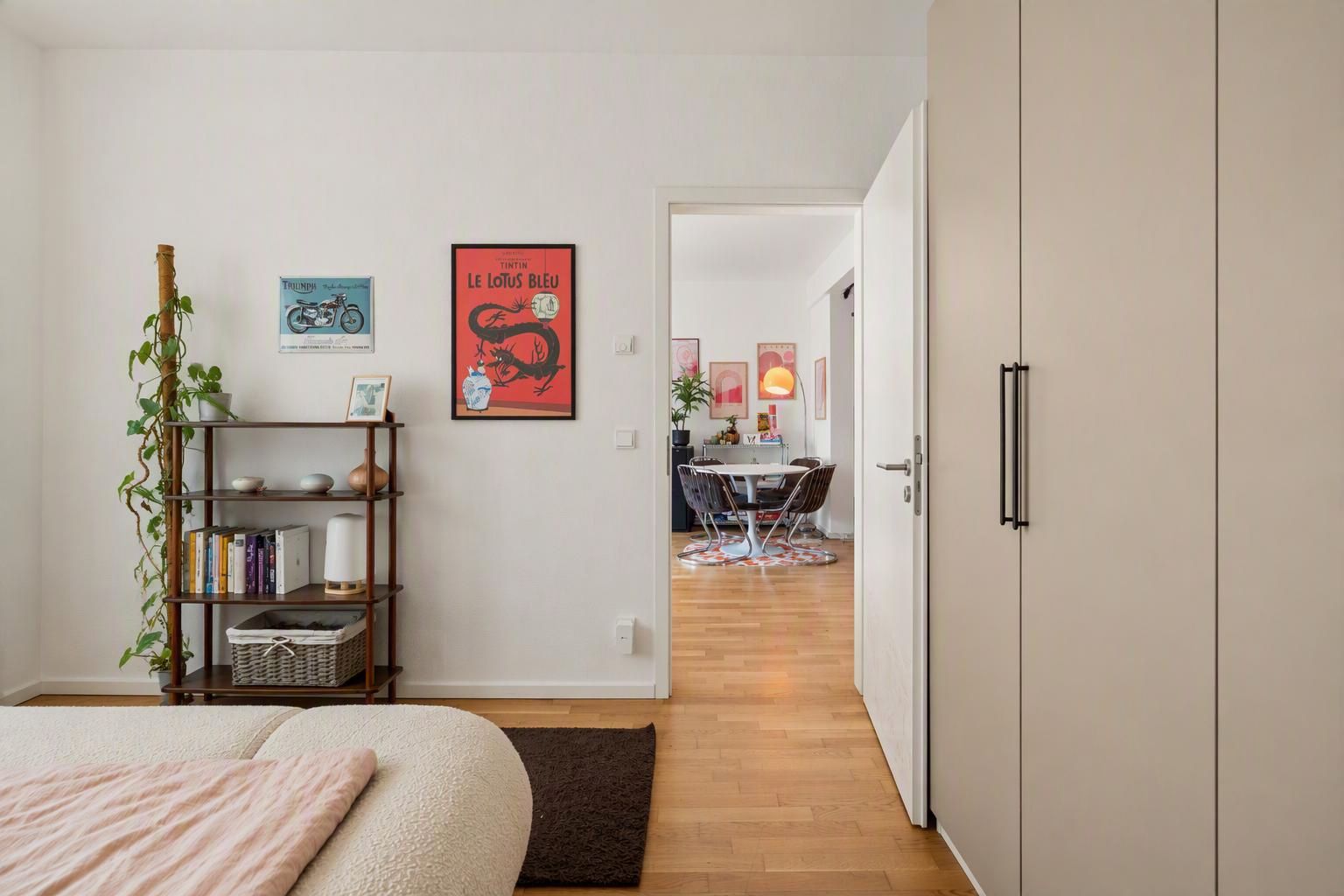Blick aus einem Schlafzimmer mit Regal, Kleiderschrank und geöffneter Tür in ein Esszimmer.