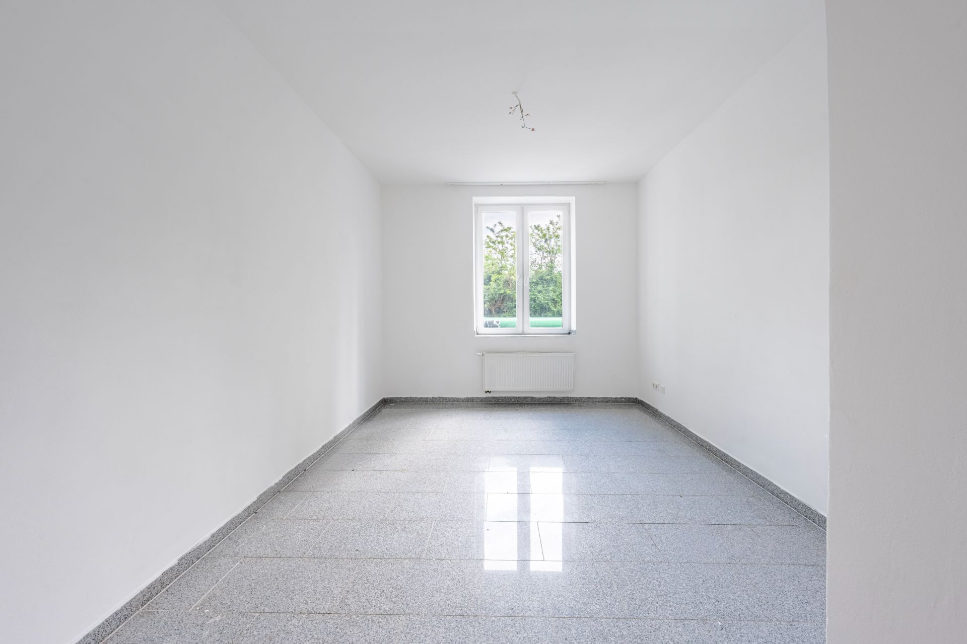Leerer, heller Raum mit weißem Wänden, großem Fenster und Fliesenboden.