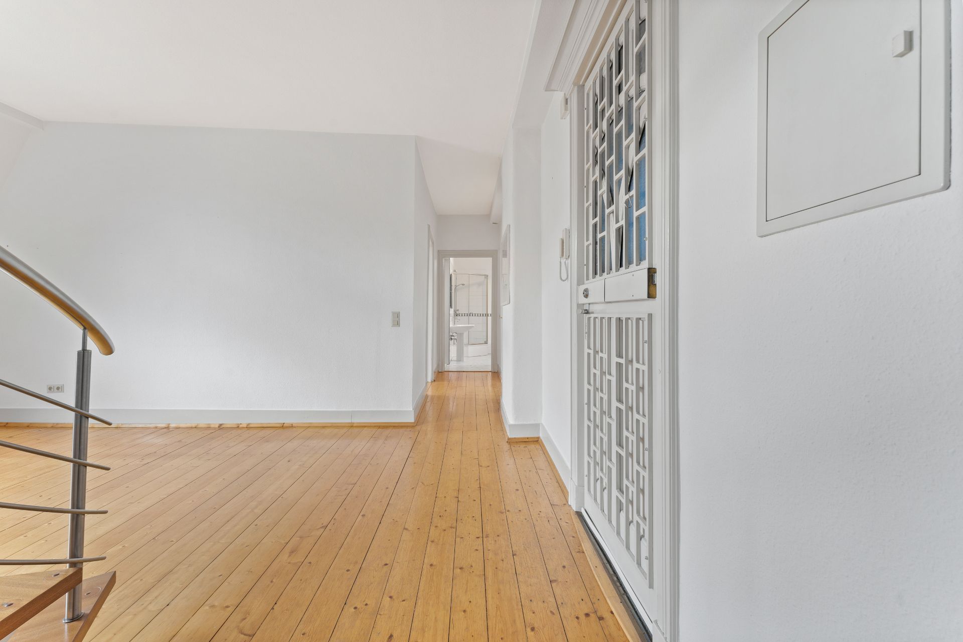 Heller Flur mit Holzfußboden, Treppengeländer und weißen Wänden in einer Wohnung.
