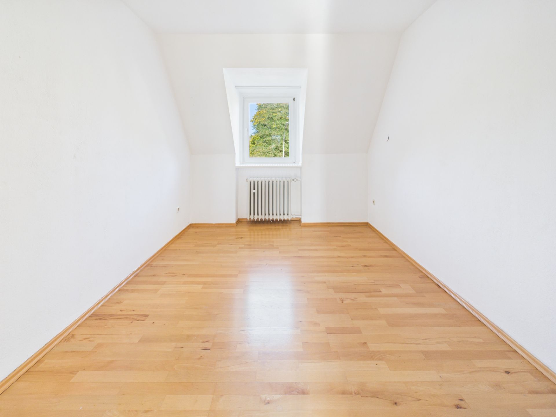 Leerer Raum mit Holzfußboden, weiß gestrichenen Wänden und Fenster mit Heizkörper.