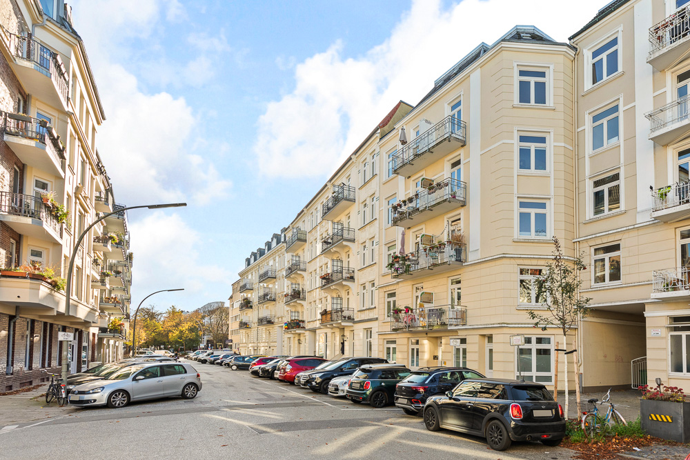 Mehrstöckige Wohnhäuser mit Balkonen an einer Straße, Autos parken am Straßenrand.