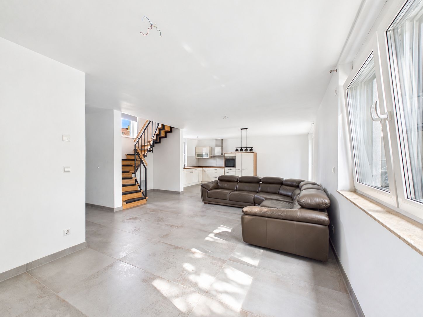 Helles Wohnzimmer mit braunem Sofa, offener Küche und Treppe nach oben.