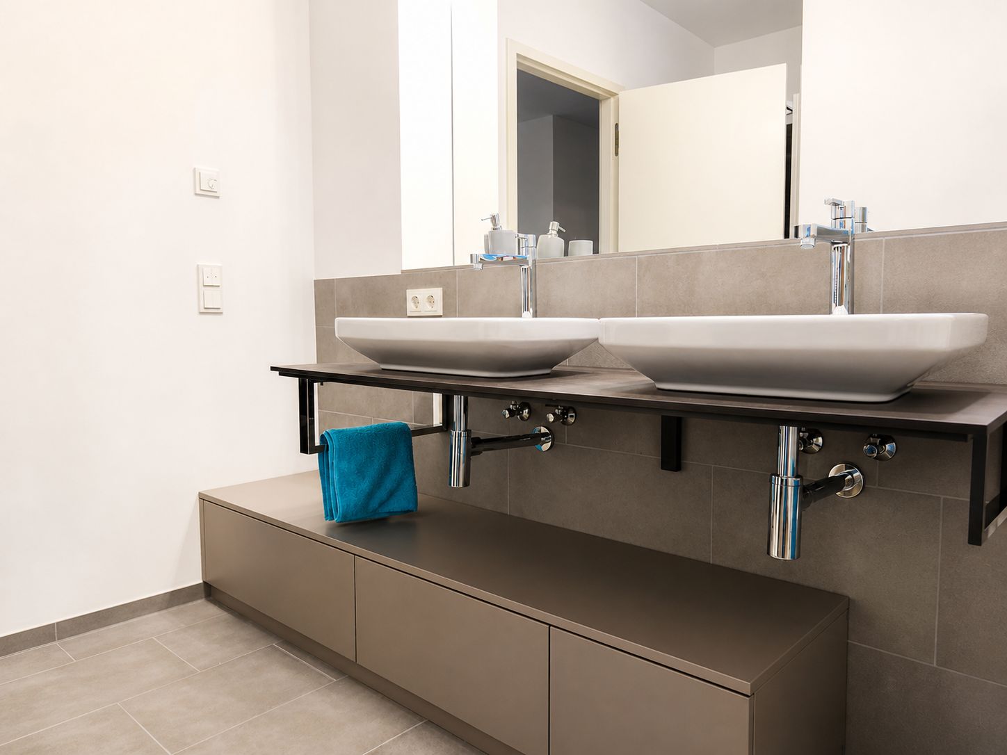 Modernes Badezimmer mit zwei Waschbecken, großem Spiegel und blauem Handtuch auf dem Unterschrank.