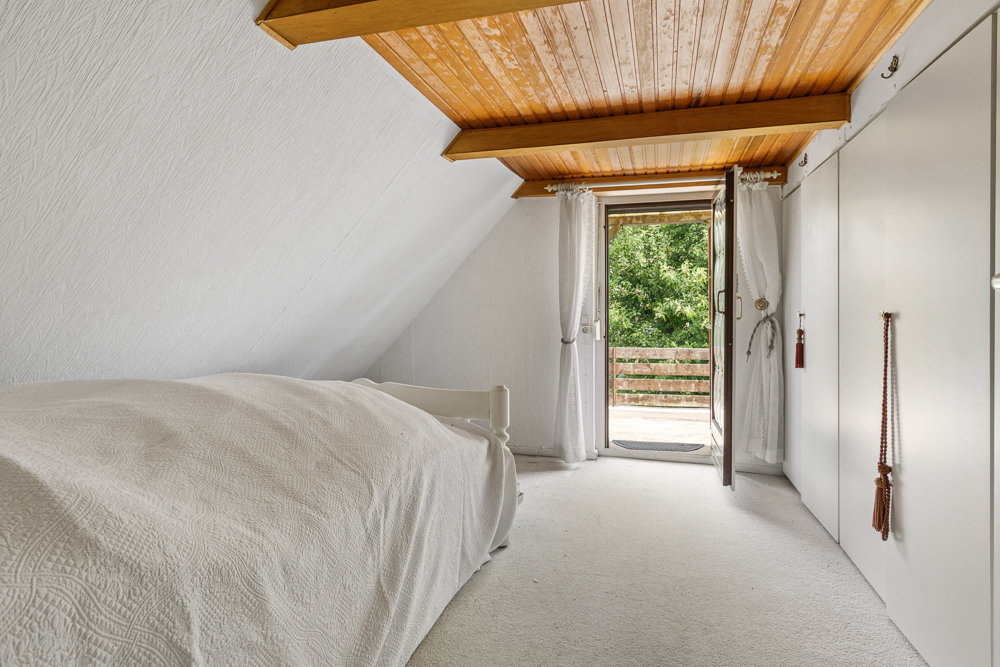 Helles Schlafzimmer mit Einzelbett, weißem Teppich und offener Tür zum Balkon.