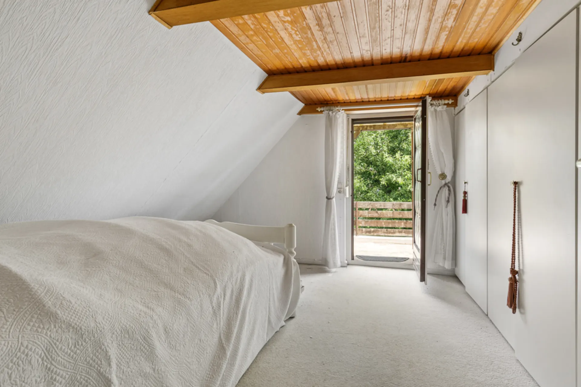 Helles Schlafzimmer mit Einzelbett, weißem Teppich und offener Tür zum Balkon.