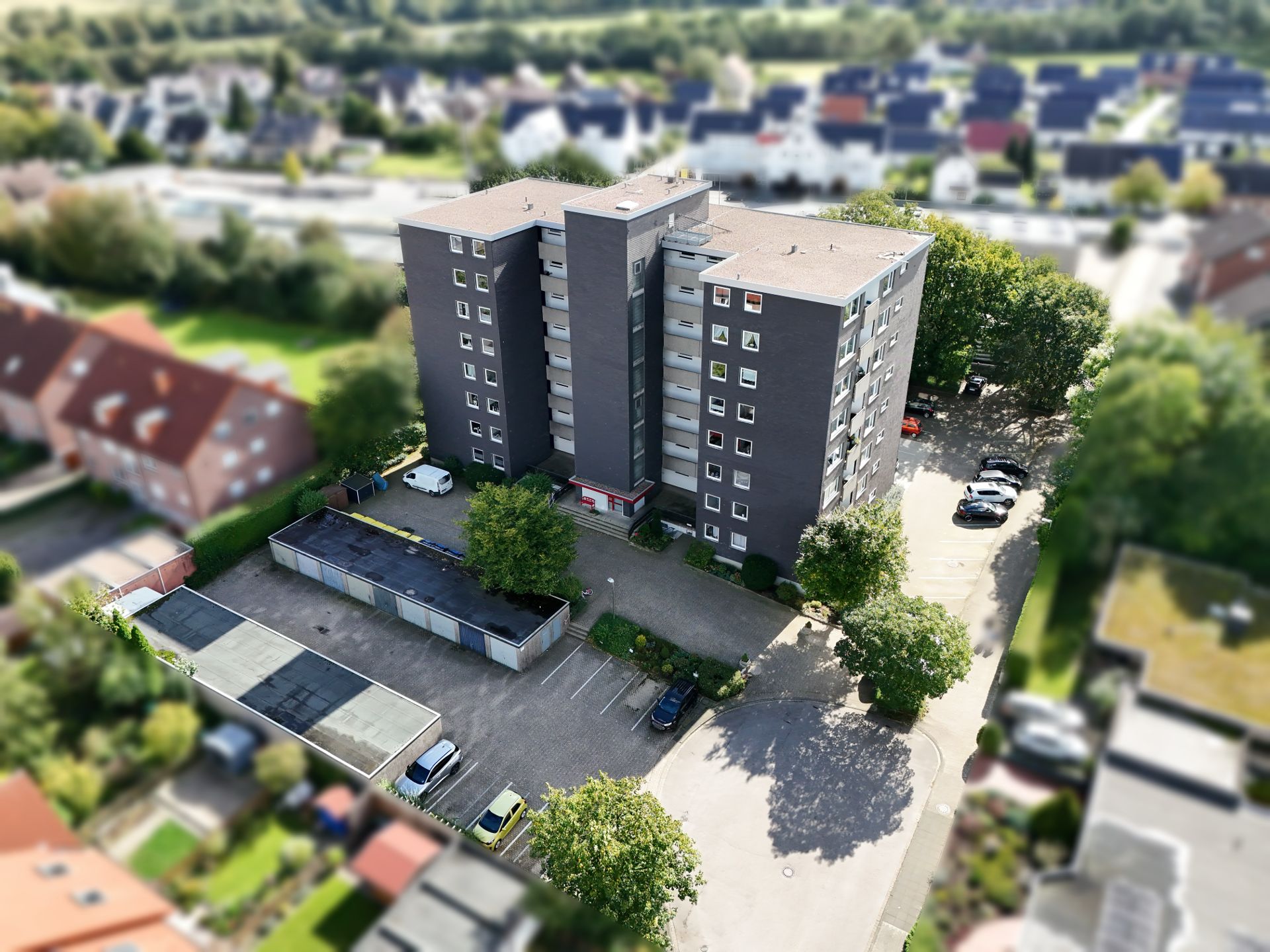 Mehrstöckiges Wohngebäude mit Parkplätzen und Bäumen, aus der Vogelperspektive aufgenommen.