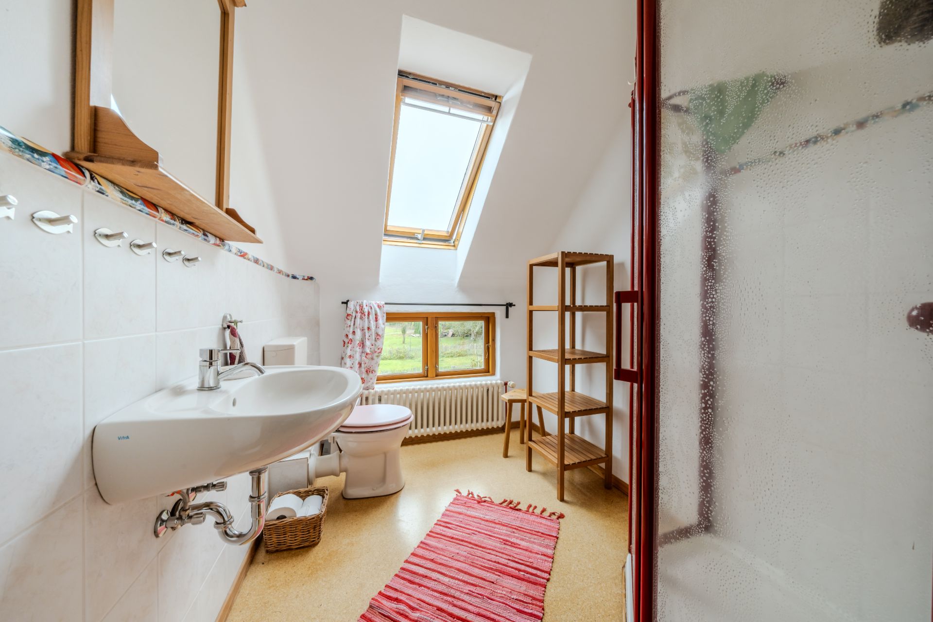 Helles Badezimmer mit Waschbecken, Toilette, Dusche, Fenster und Holzregal.