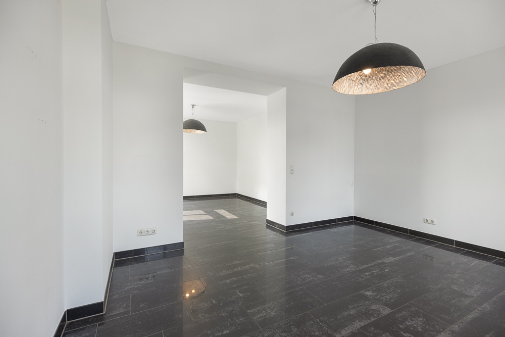 Leerer Raum mit schwarzen Fliesen, weißen Wänden und zwei schwarzen Deckenlampen.
