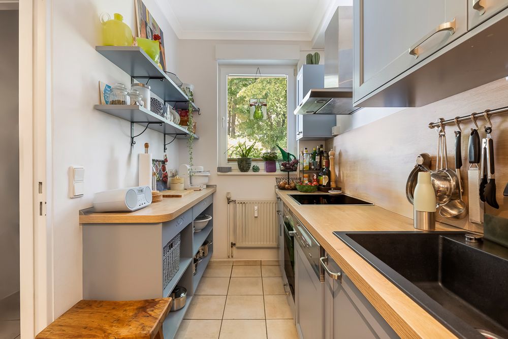 Schmale Küche mit Holzarbeitsplatten, offenen Regalen, Fenster und Küchengeräten.