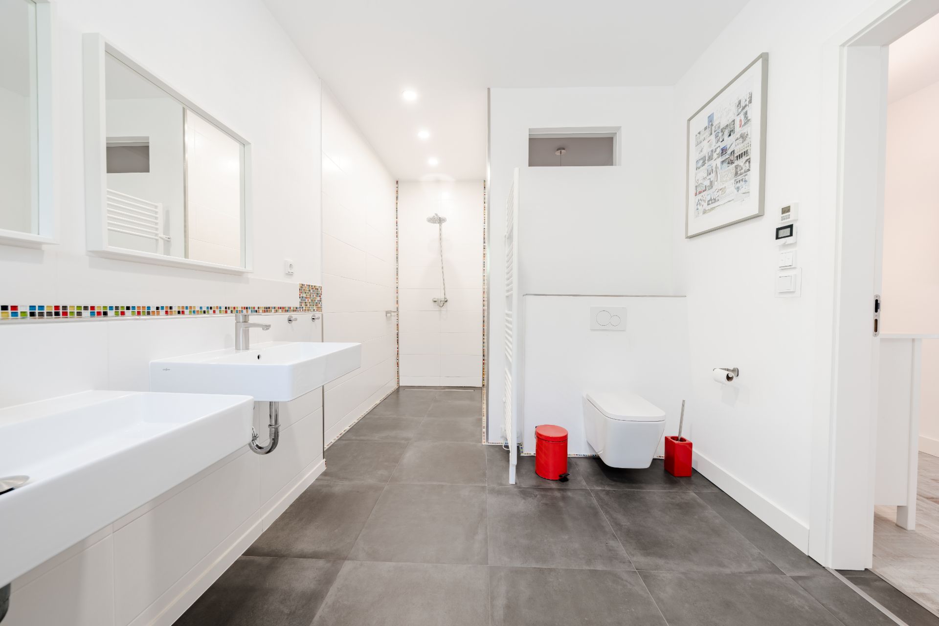 Modernes Badezimmer mit zwei Waschbecken, bodenebener Dusche, Toilette und roten Badaccessoires.