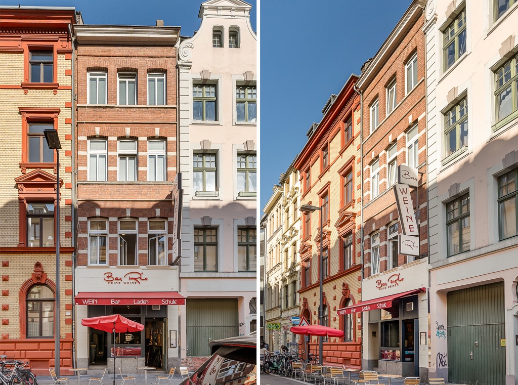 Mehrstöckiges Wohnhaus mit roter Fassade, Außencafé und Sonnenschirmen vor dem Eingang.