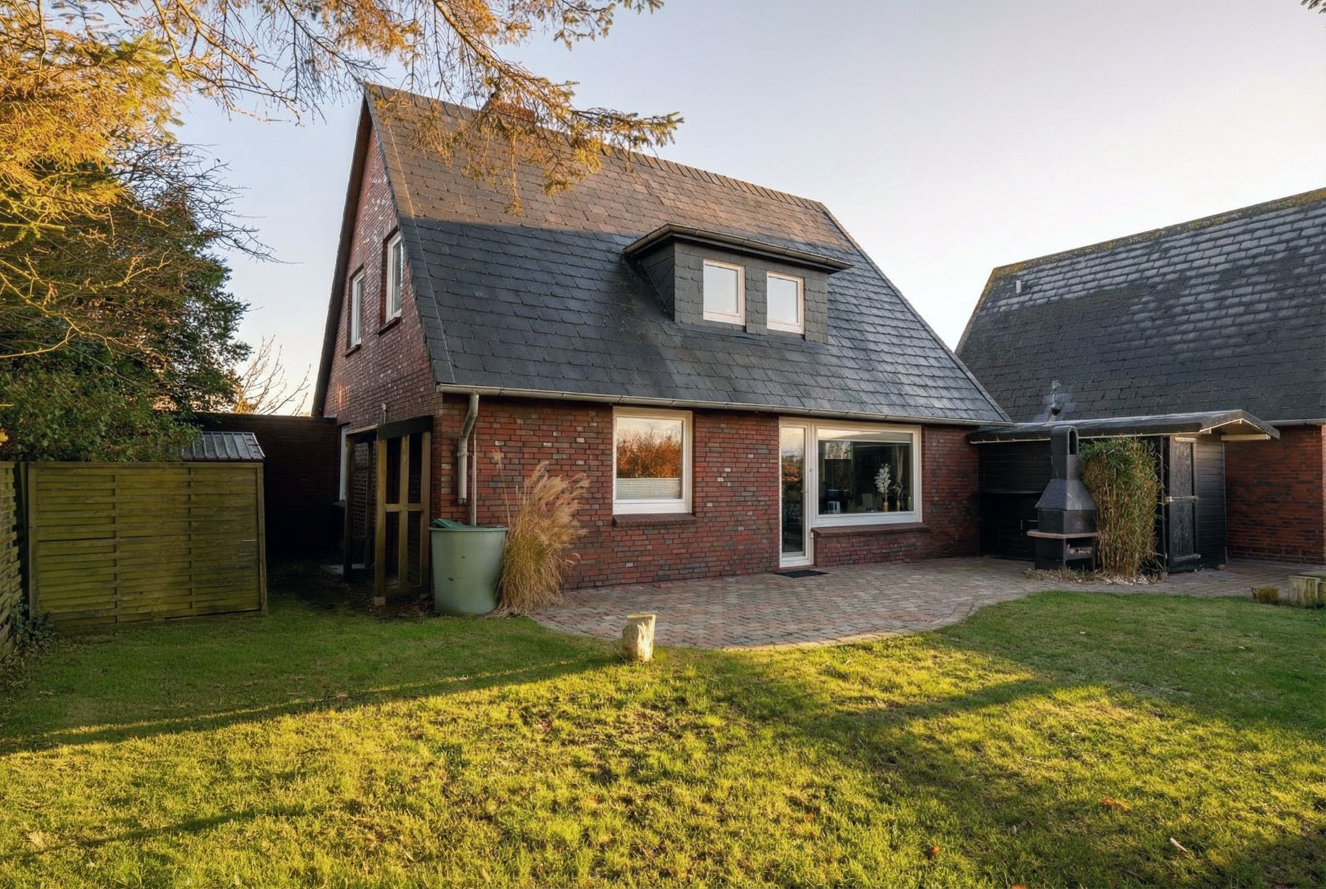Backstein-Einfamilienhaus mit großem Fenster und Garten, Terrasse mit Grill.