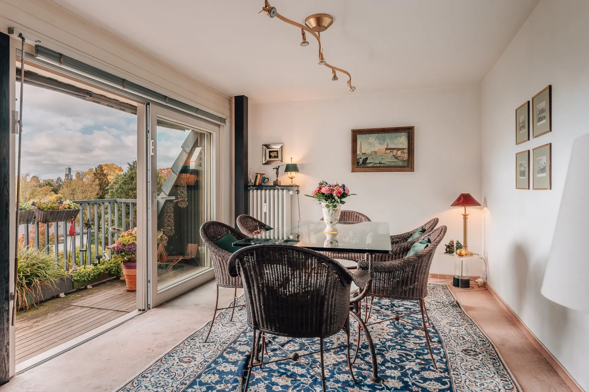 Essbereich mit Glastisch, vier Korbstühlen und Zugang zum Balkon mit Pflanzen.