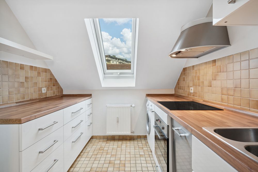 Helle Küche mit Schrägdach, Fenster, weißen Schränken und Holzarbeitsplatten.