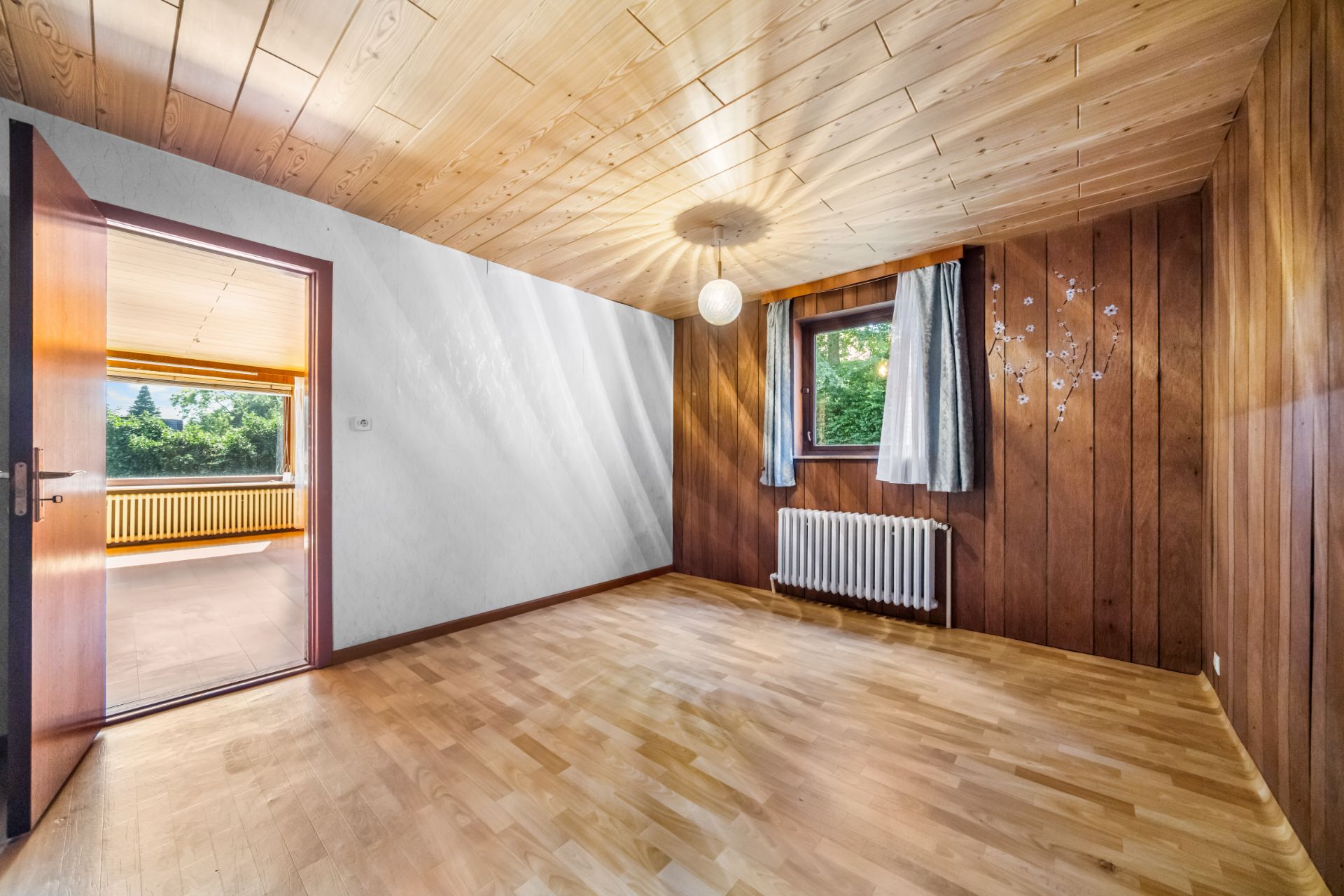 Leerer Raum mit Holzdecke, Holzverkleidung, Fenster mit Vorhängen und offenem Durchgang.