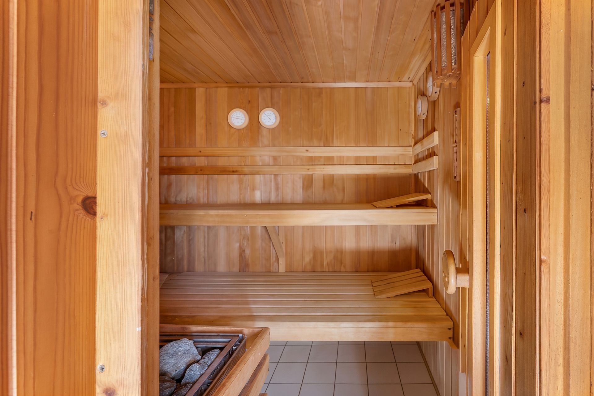 Holzsauna mit zwei Bänken, Saunaofen und gefliester Boden.