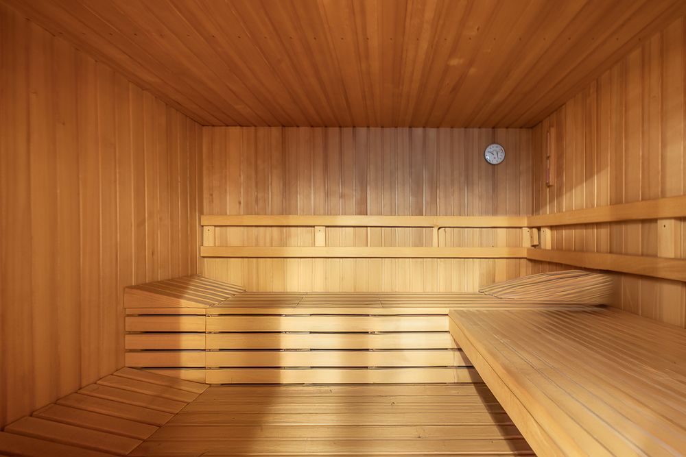 Innenansicht einer holzverkleideten Sauna mit zwei Holzbänken und einer Uhr an der Wand.