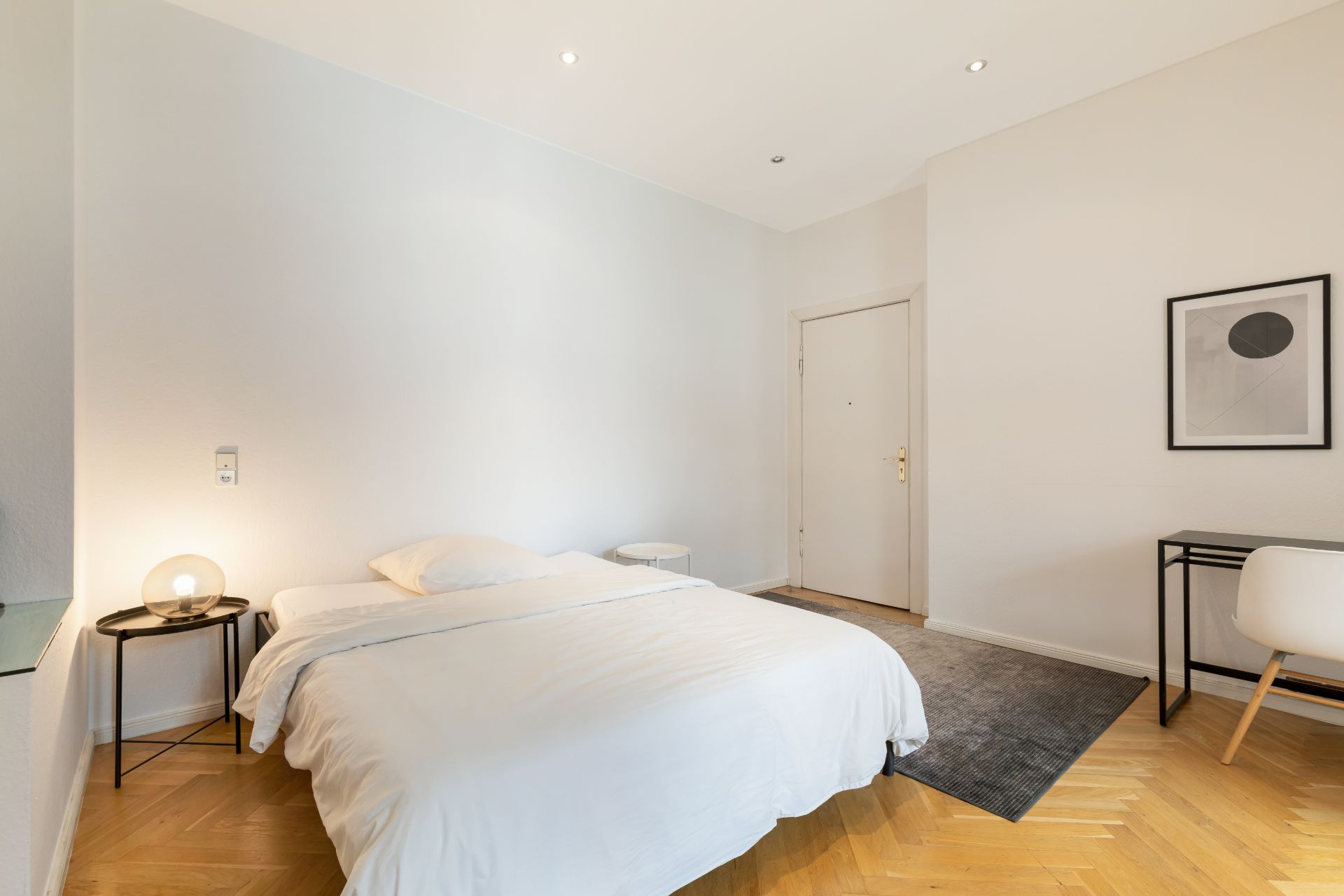 Helles Schlafzimmer mit Doppelbett, Nachttischen, Schreibtisch und Stuhl auf Holzboden.