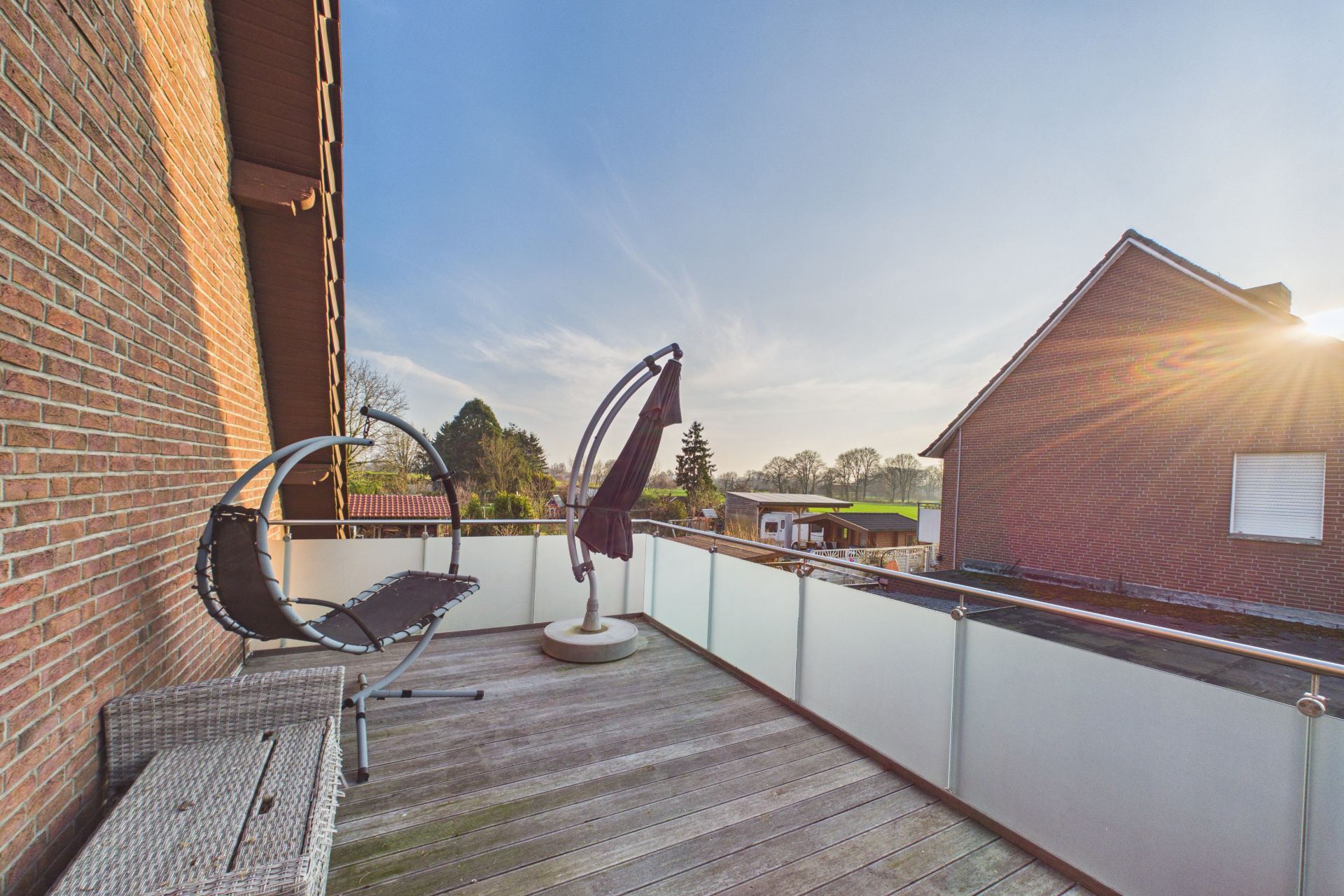 Großer Balkon mit Holzfußboden, Hängesessel und Rattanbank, Ausblick auf Nachbarhäuser.