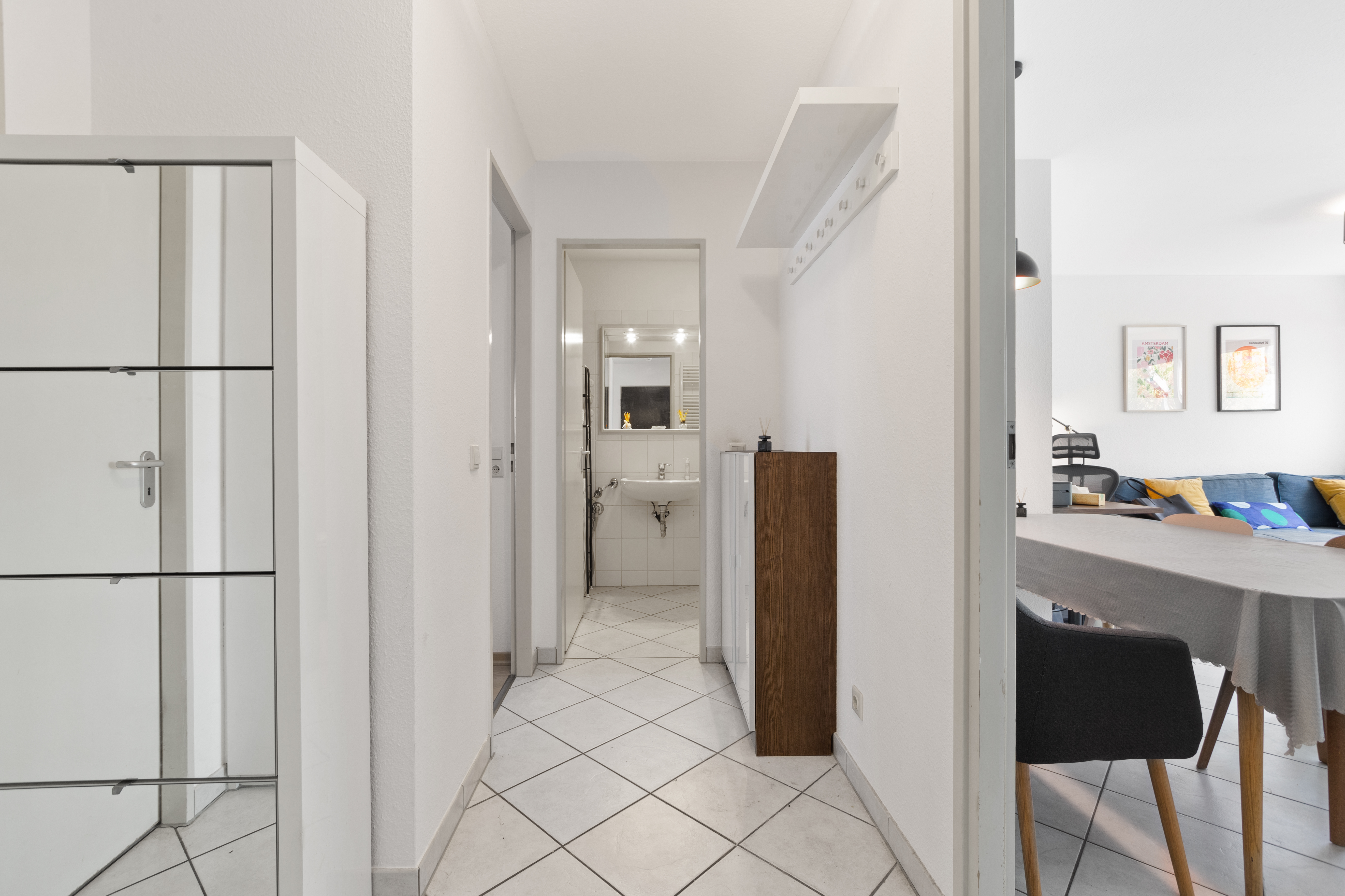 Heller Flur mit Fliesenboden, Blick ins Badezimmer und angrenzendem Wohnzimmer mit Esstisch.