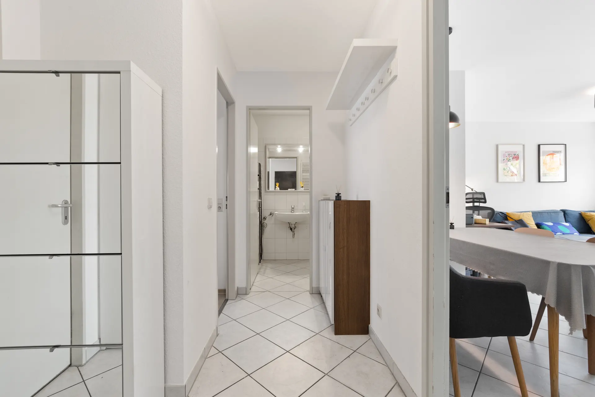 Heller Flur mit Fliesenboden, Blick ins Badezimmer und angrenzendem Wohnzimmer mit Esstisch.