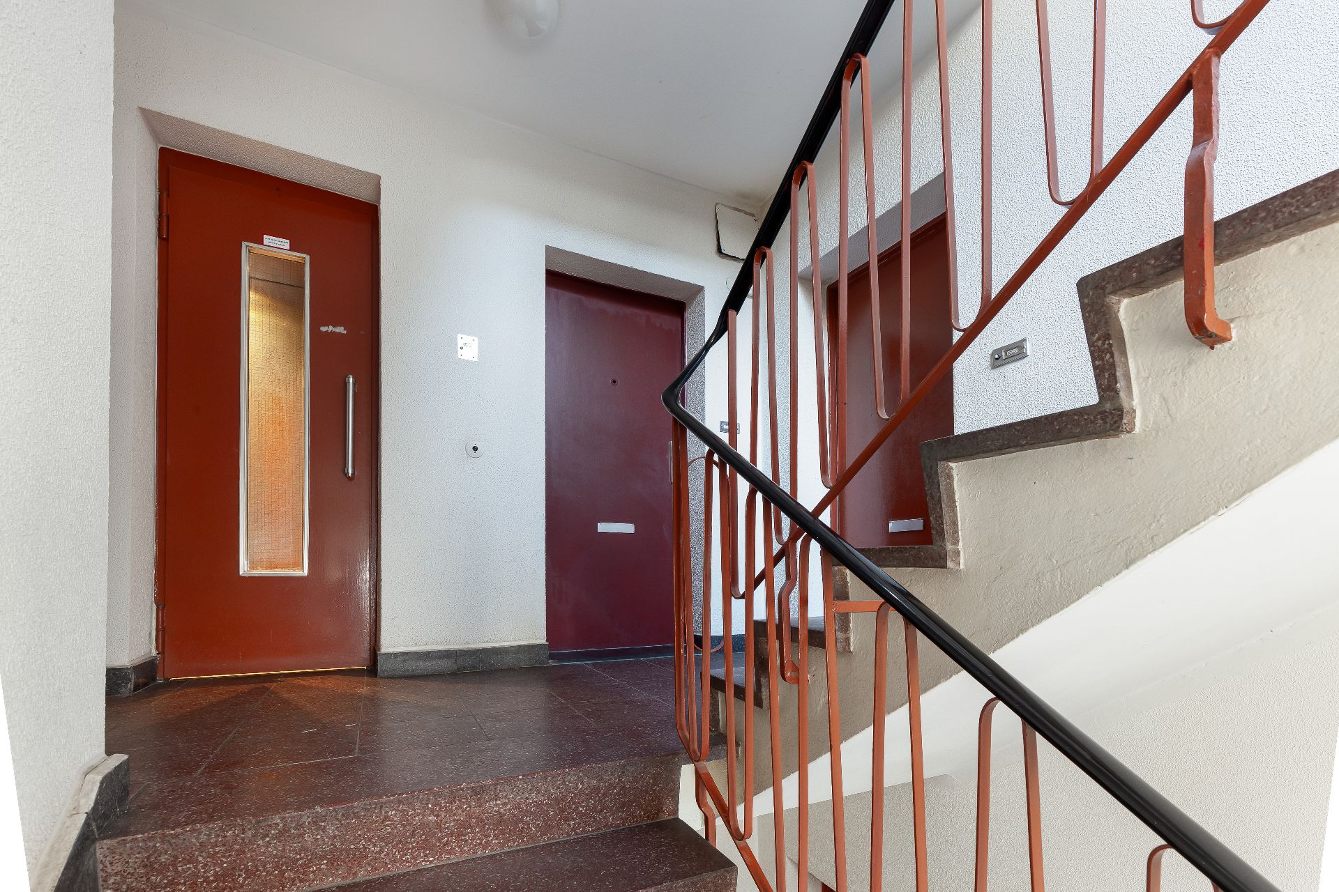Treppenhaus mit braunen Türen und roten Geländern in einem Wohngebäude.