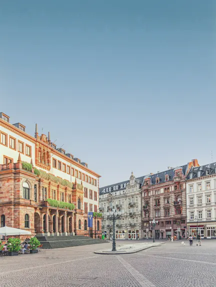 Historische Wohngebäude an einem großen, gepflasterten Platz bei Tageslicht.
