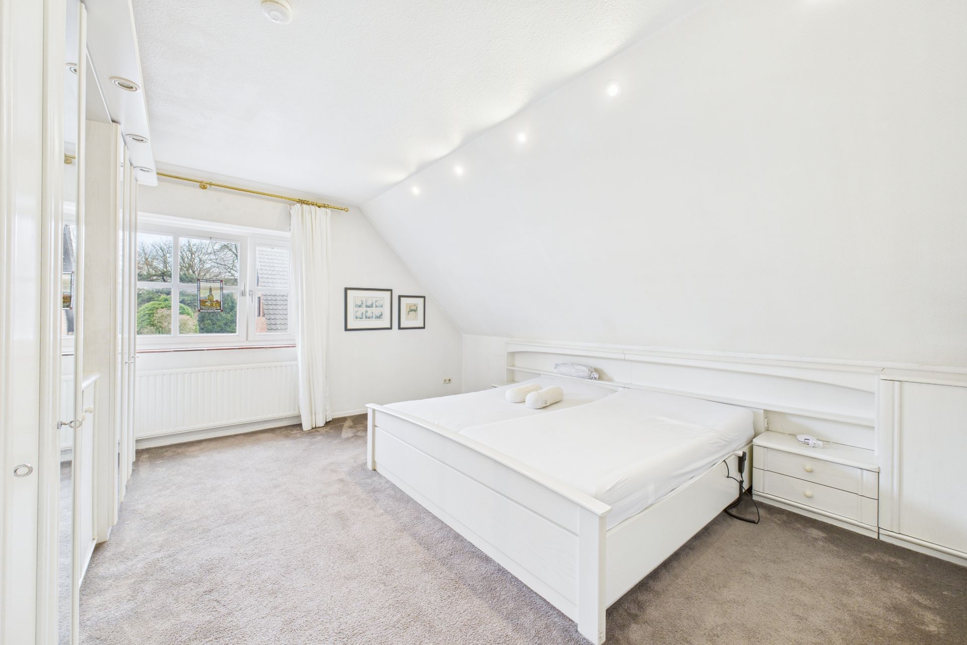 Helles Schlafzimmer mit Doppelbett, Nachttischen und großem Fenster mit Vorhängen.