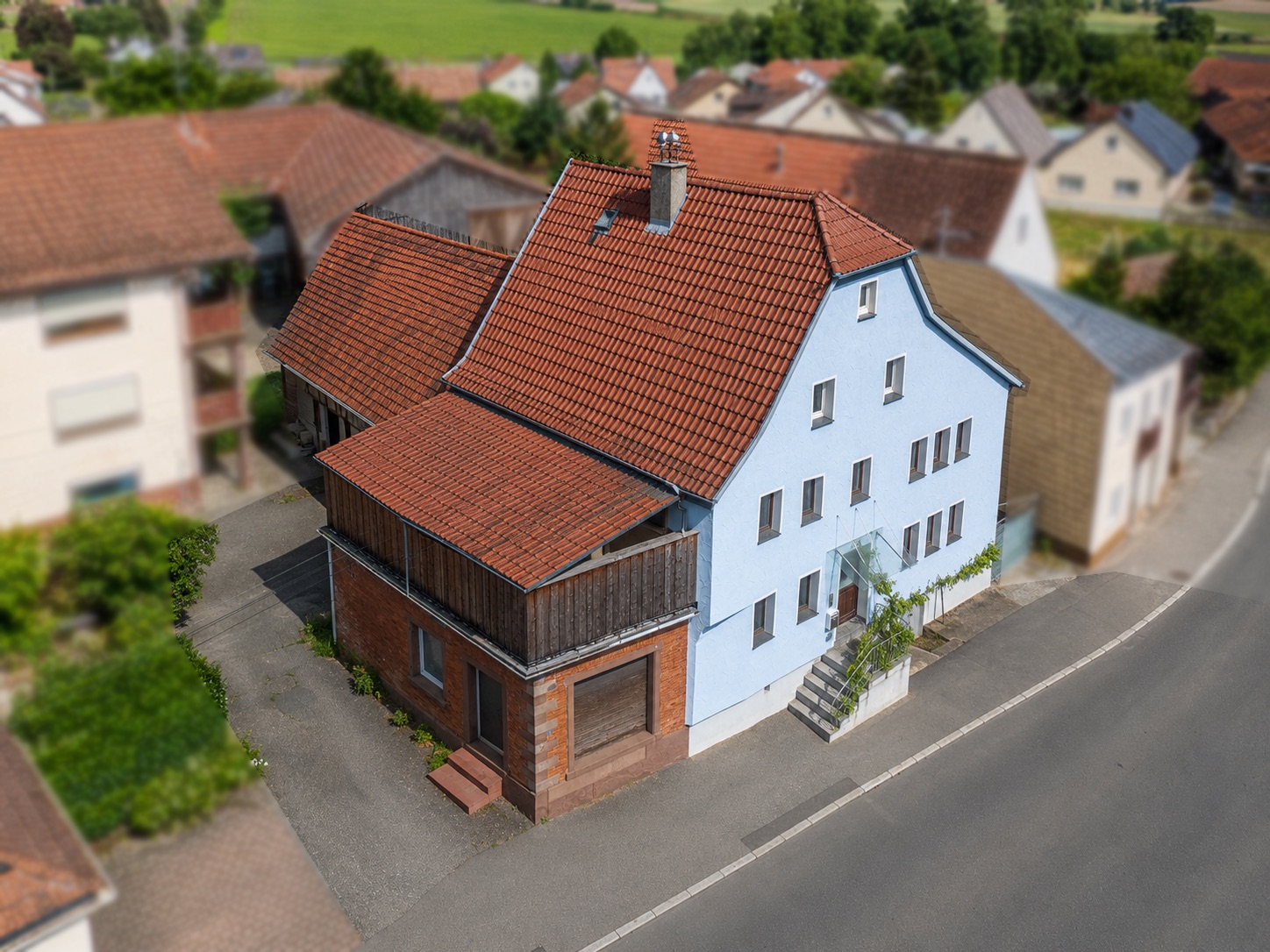 Zweistöckiges Wohnhaus mit rotem Dach und blauer Fassade an einer Straßenecke.