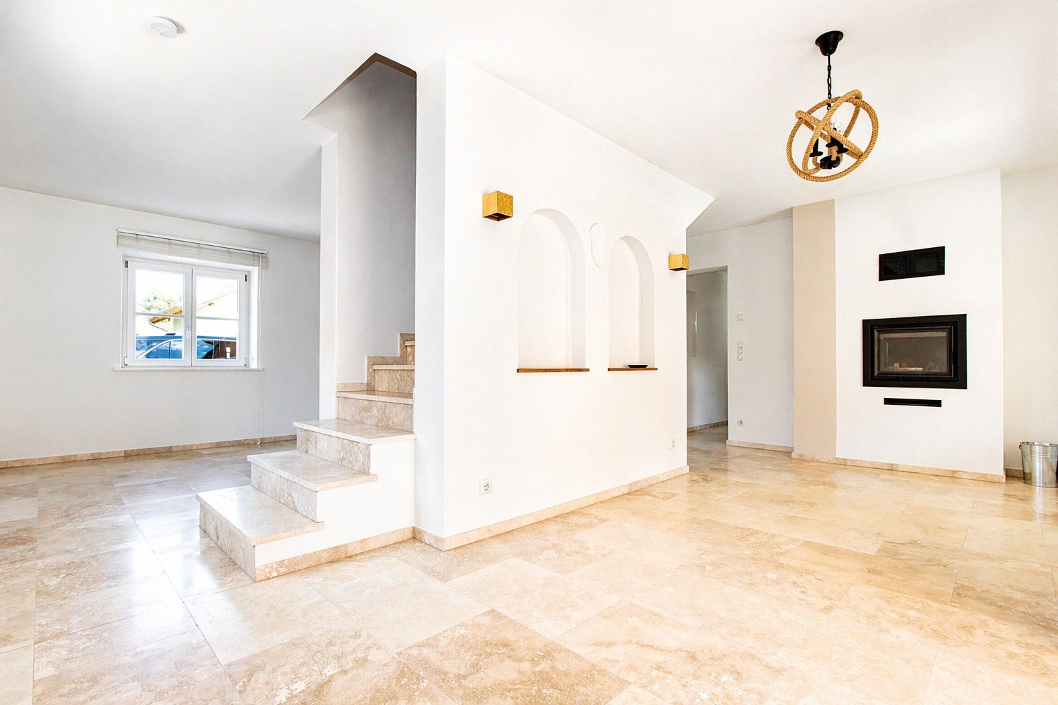 Helles Wohnzimmer mit offenem Kamin, Treppe und großen Fenstern.