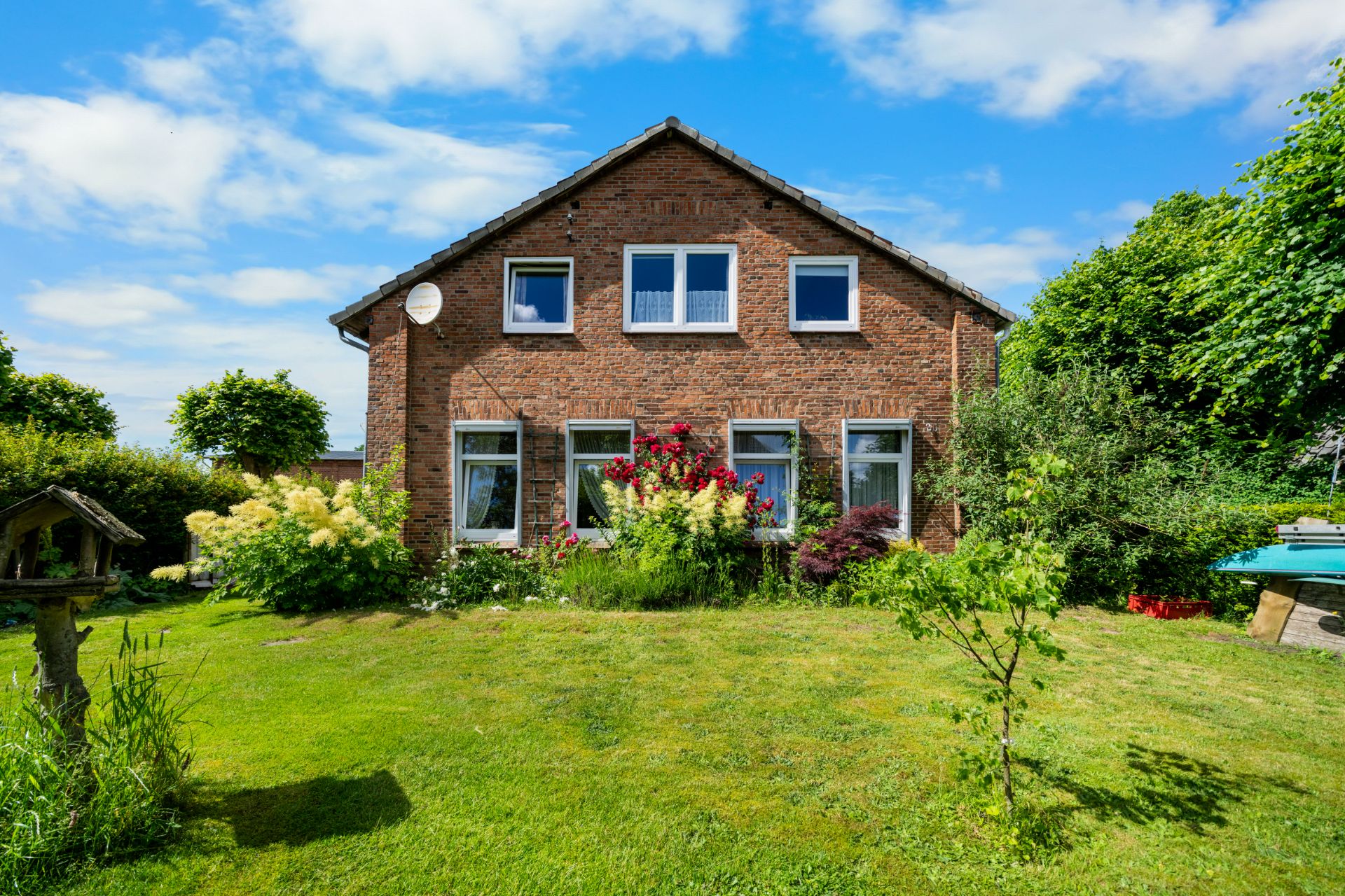 Backsteinwohnhaus mit fünf Fenstern und gepflegtem Garten im Vordergrund.