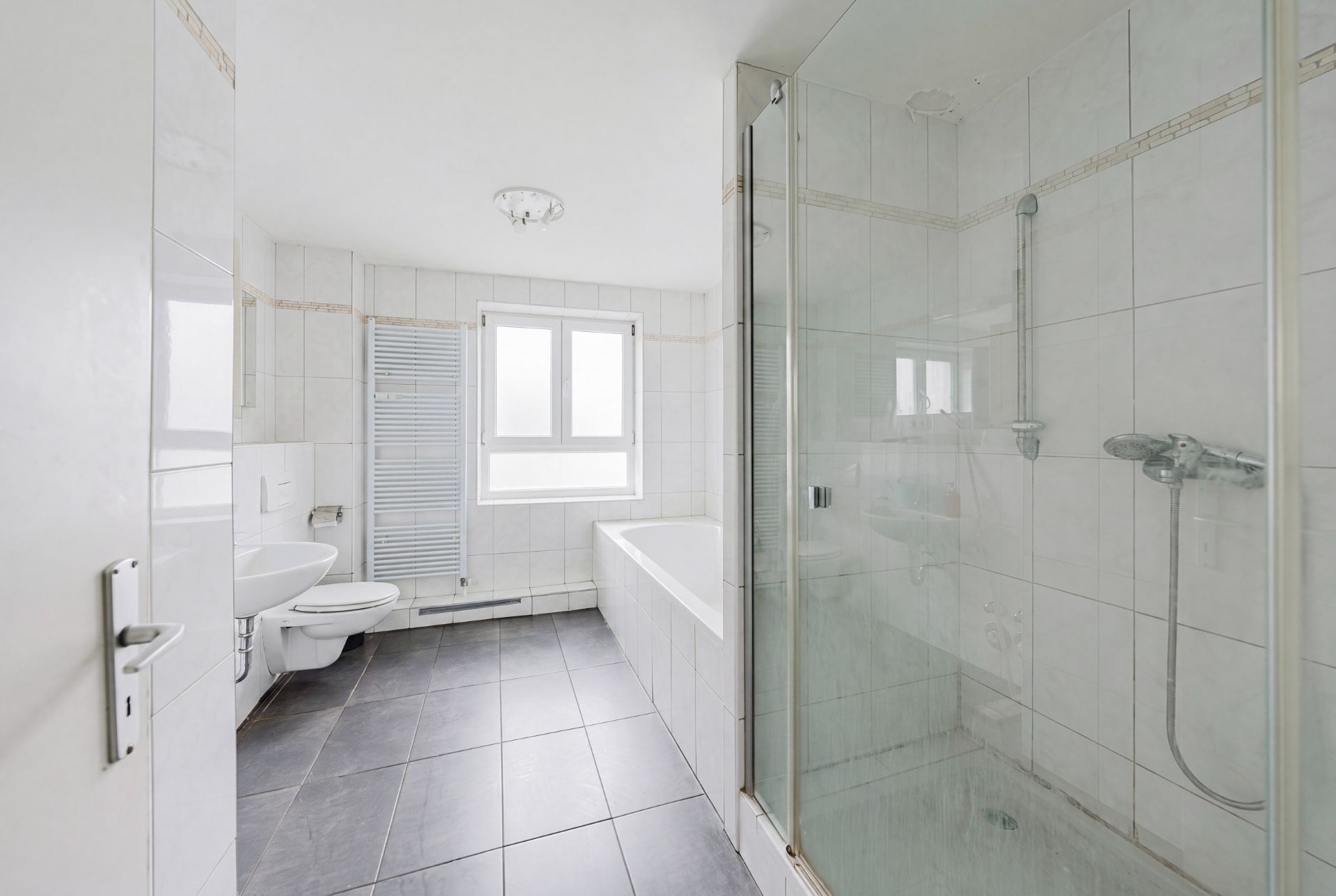 Helles Badezimmer mit Dusche, Badewanne, WC, Waschbecken und Fenster.