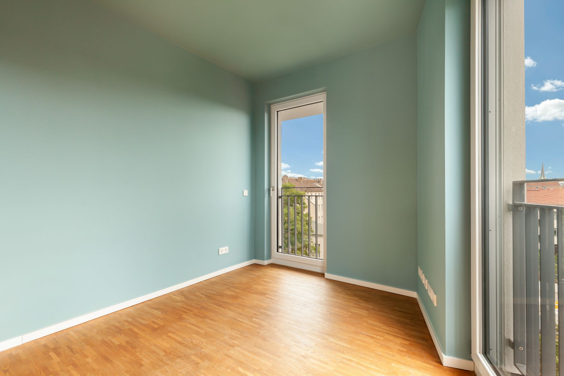 Leerer Raum mit hellblauen Wänden, Holzboden und Tür zu einem Balkon.