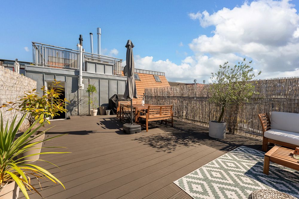 Große Dachterrasse mit Holzboden, Sitzmöbeln, Topfpflanzen und Sonnenschirm.