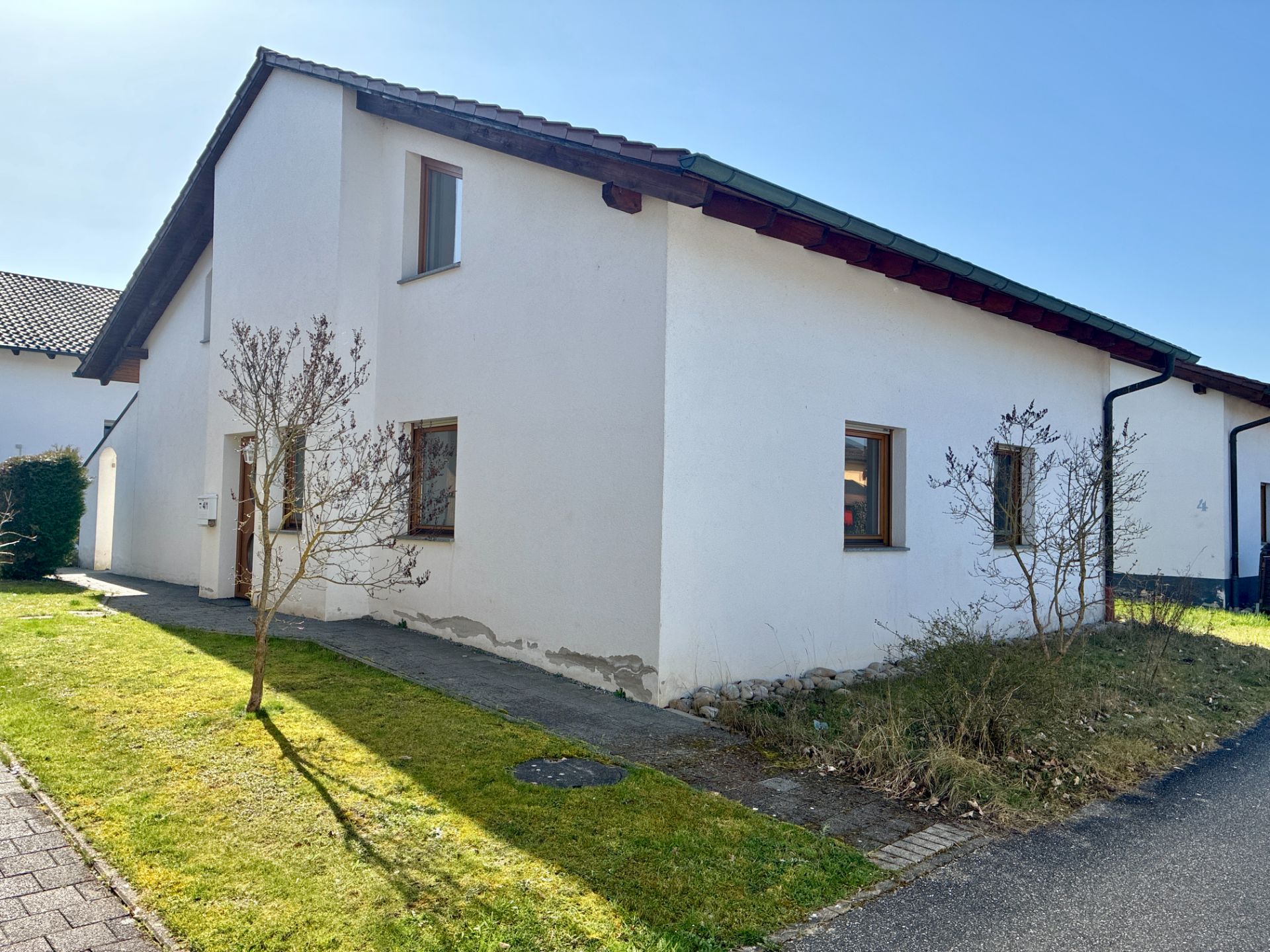 Weißes Einfamilienhaus mit Garten und Gehweg, zwei kleine Bäume vor dem Haus.