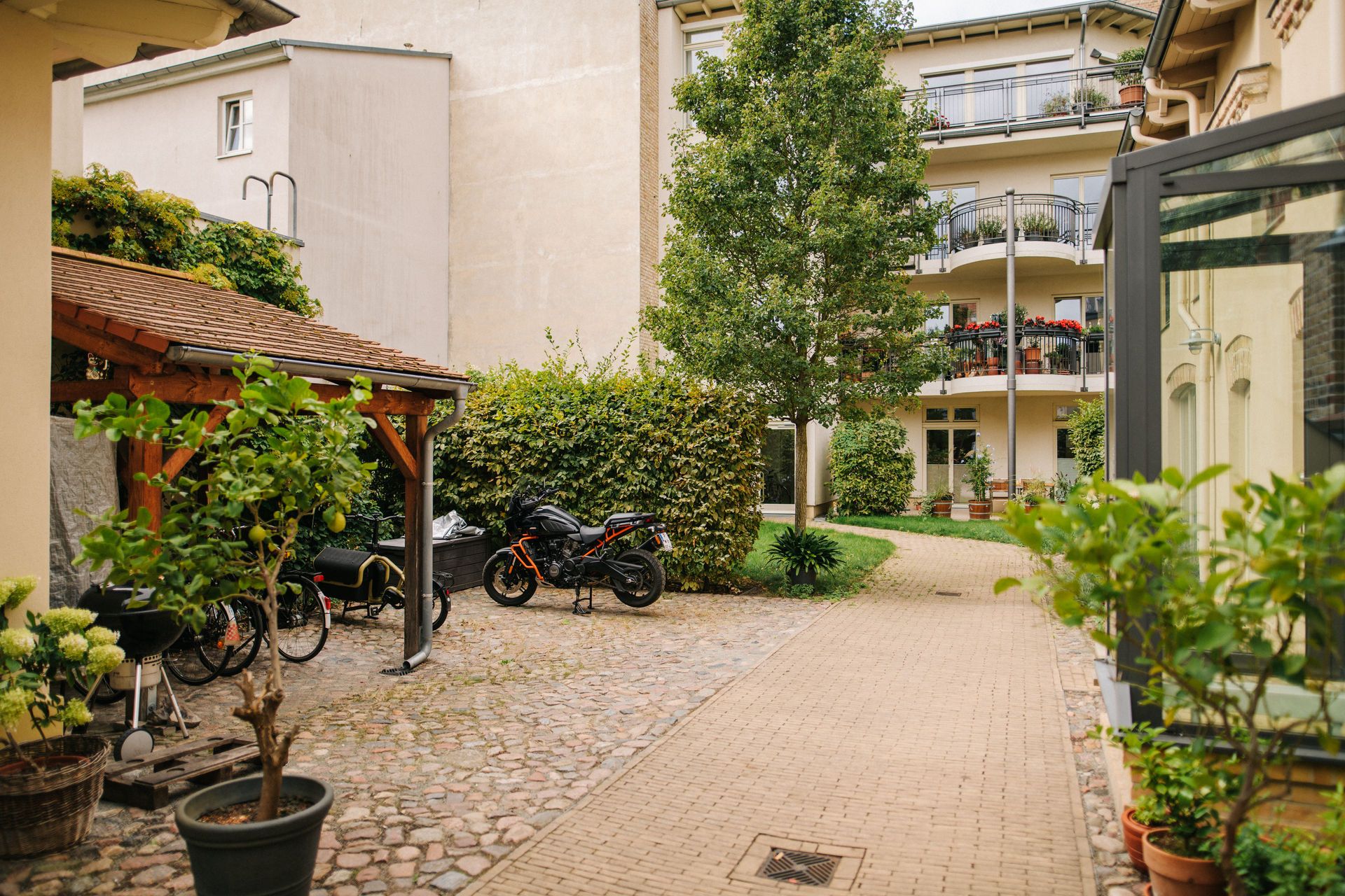 Innenhof mit Bäumen, Fahrrädern, Motorrädern und einem mehrstöckigen Wohnhaus mit Balkonen.