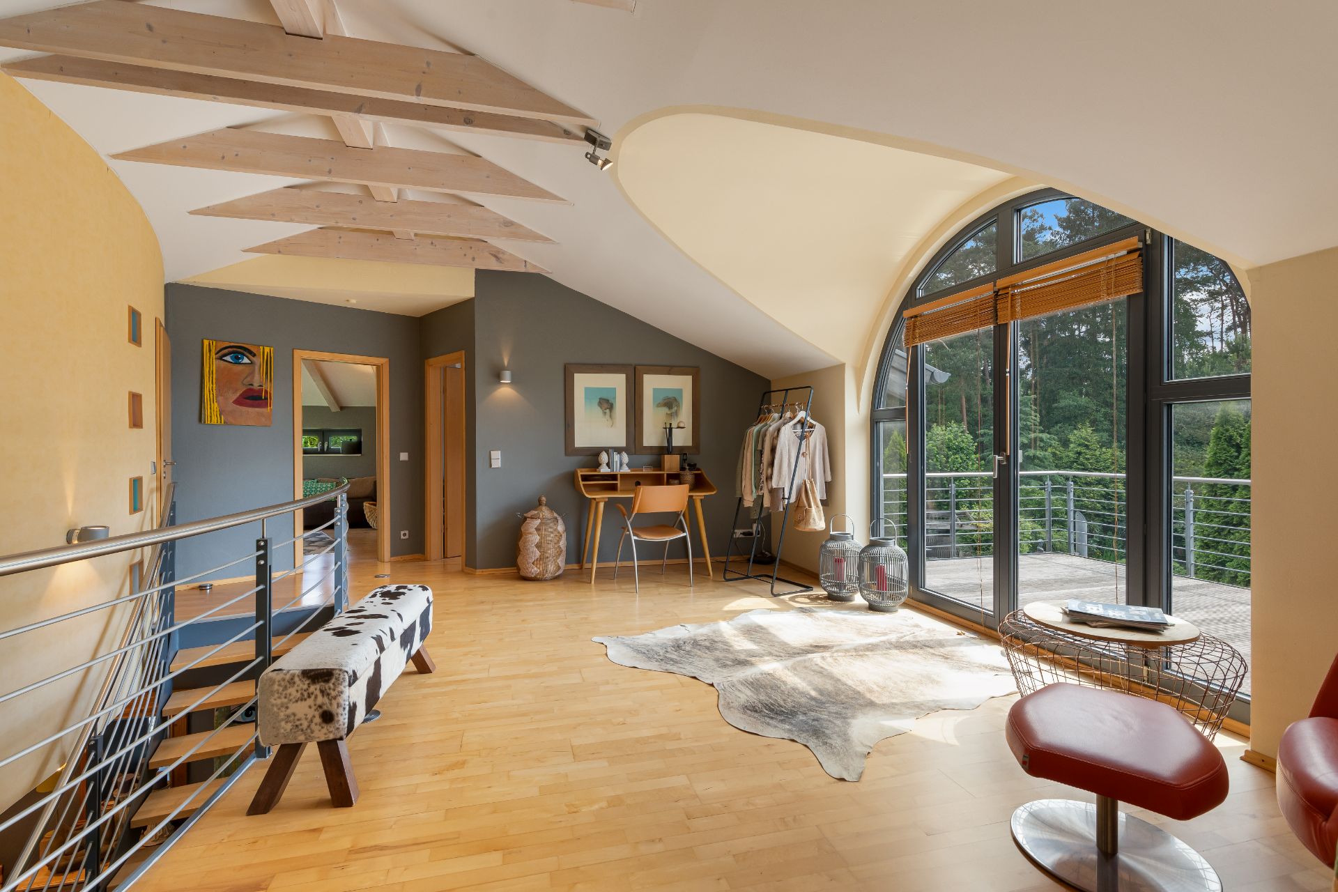 Helles Zimmer mit Holzfußboden, großen Fenstern, Sitzbereich und Schreibtisch, Blick ins Grüne.