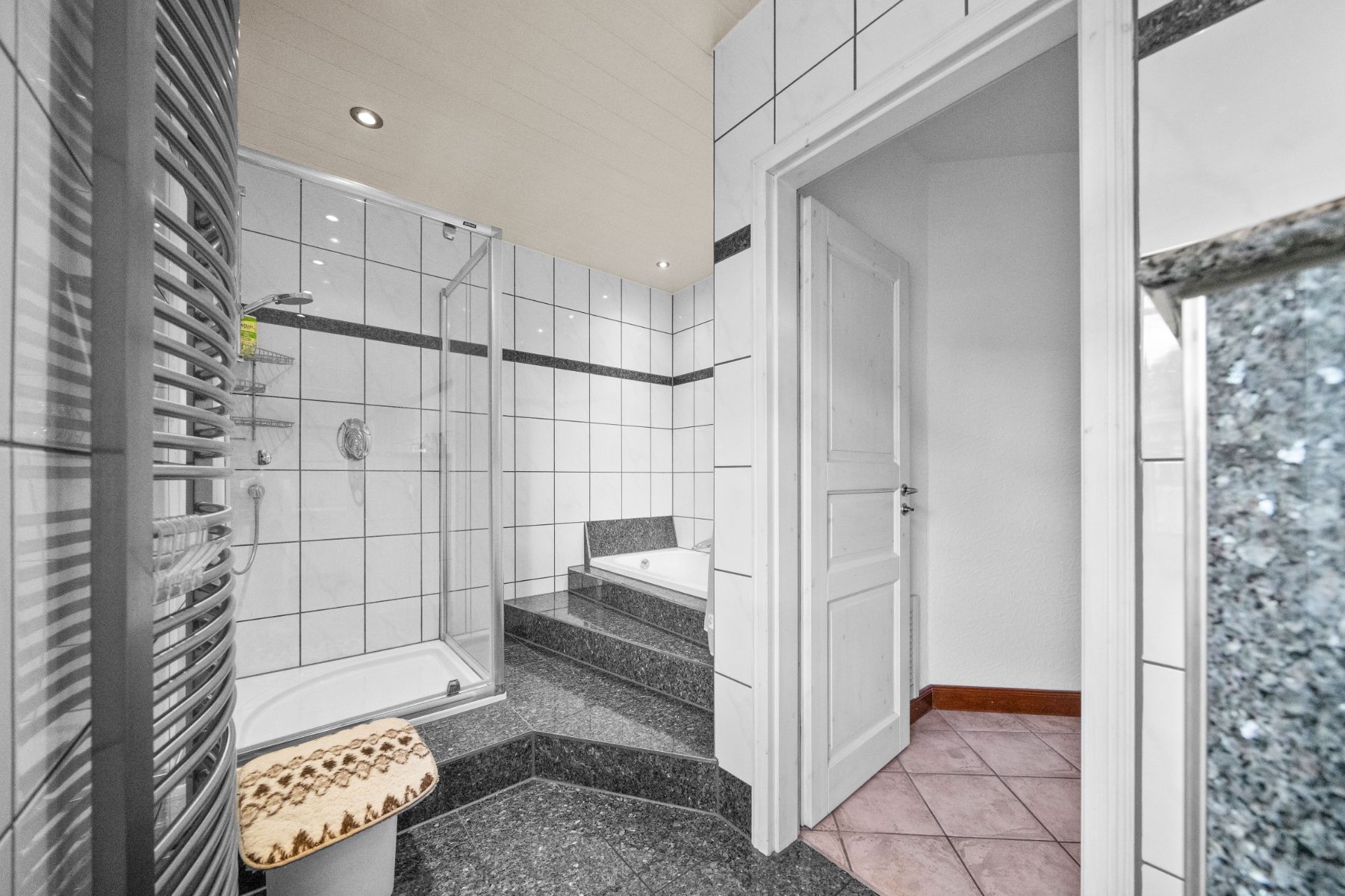 Modernes Bad mit Dusche, Badewanne auf Stufe, Handtuchheizkörper und weiß gefliesten Wänden.